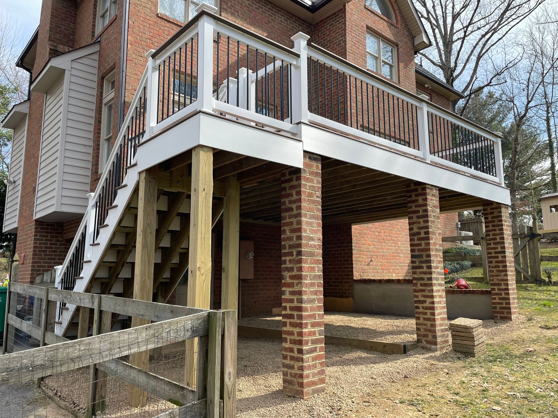 Brick house with a raised wooden deck and stairs supported by brick pillars, viewed from the yard