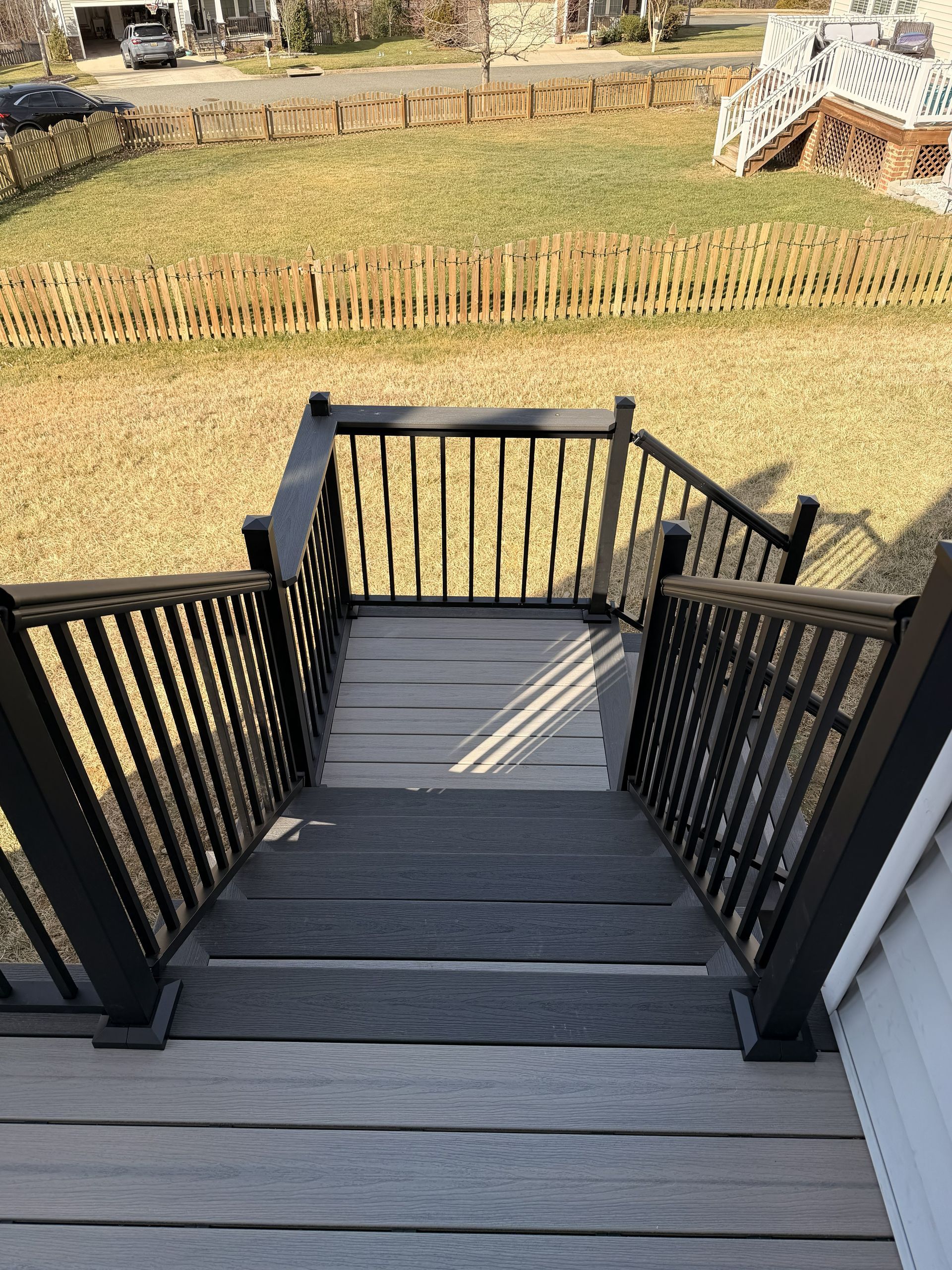 Wooden deck stairs with black railings leading down to a grassy yard and fenced garden area