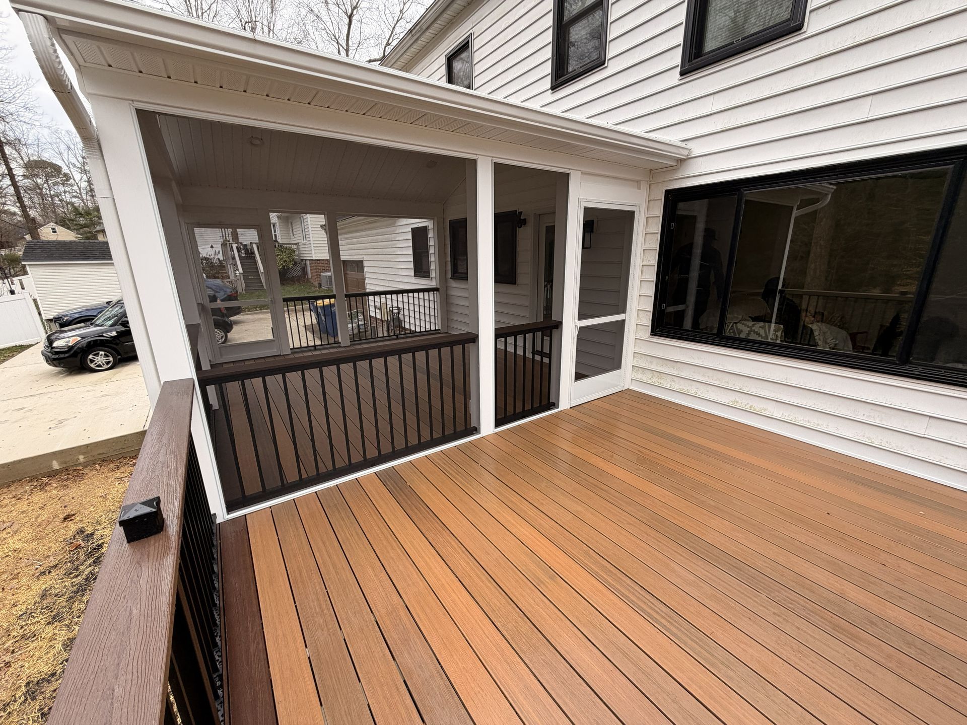 Covered wooden deck with white railings and a screened porch beside a house