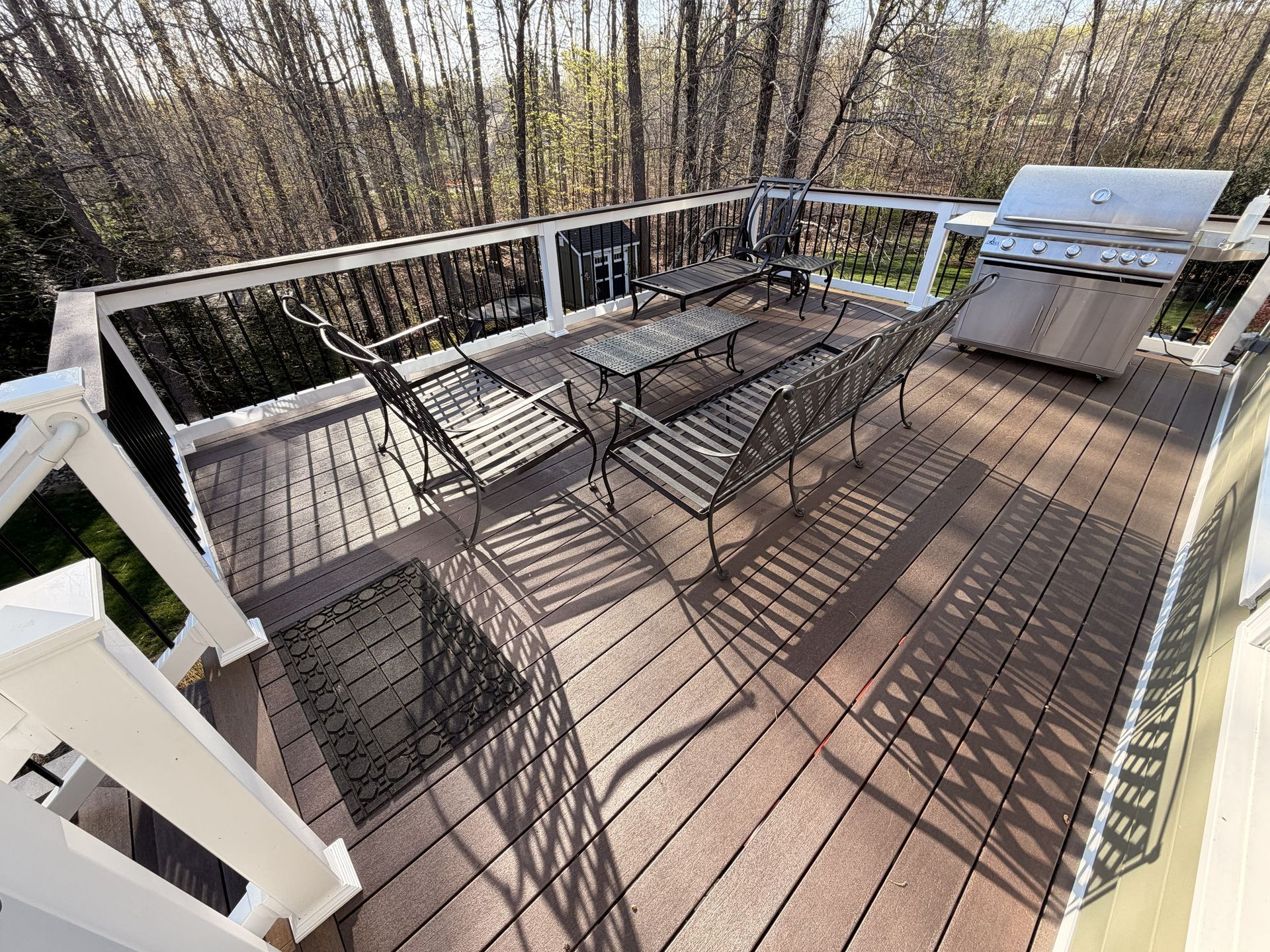 Wooden deck with glass-top patio table, chairs, and a grill overlooking bare trees