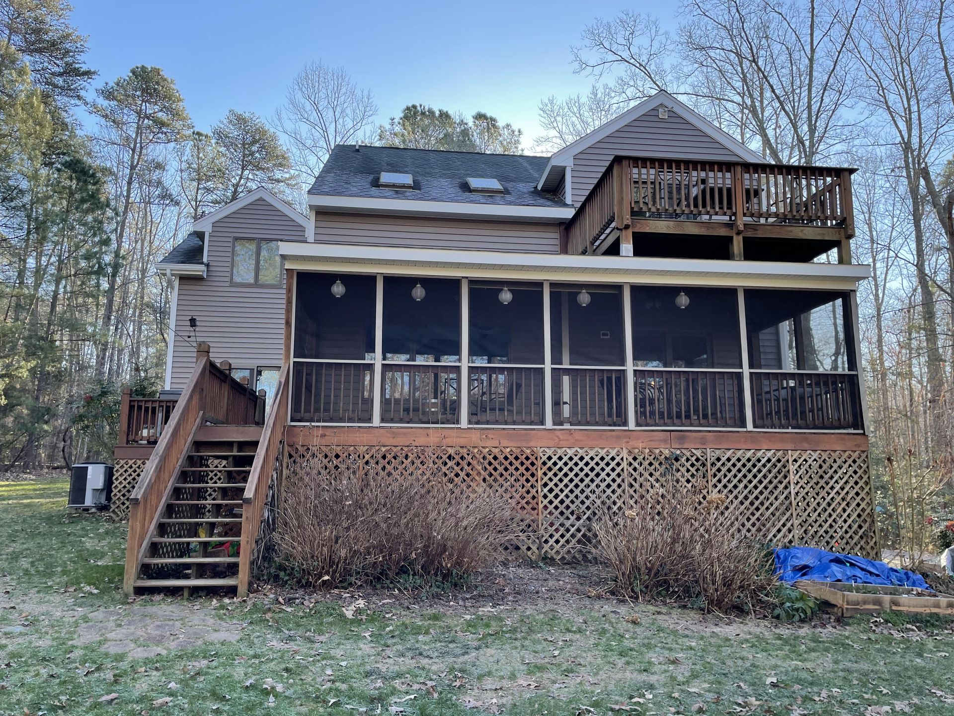 Wooden house with screened porch, exterior stairs, and deck in a wooded yard.