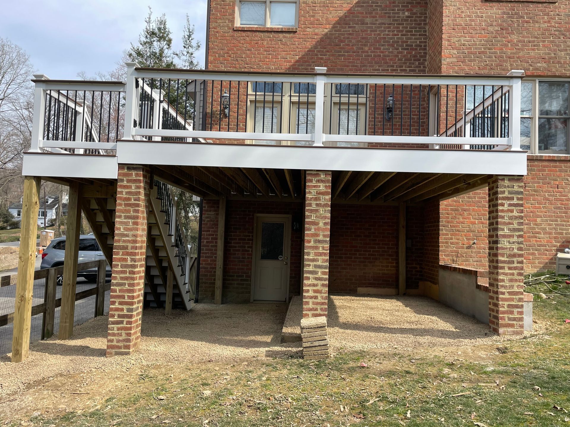 Elevated brick house with a white-railed deck, covered patio, and support columns underneath