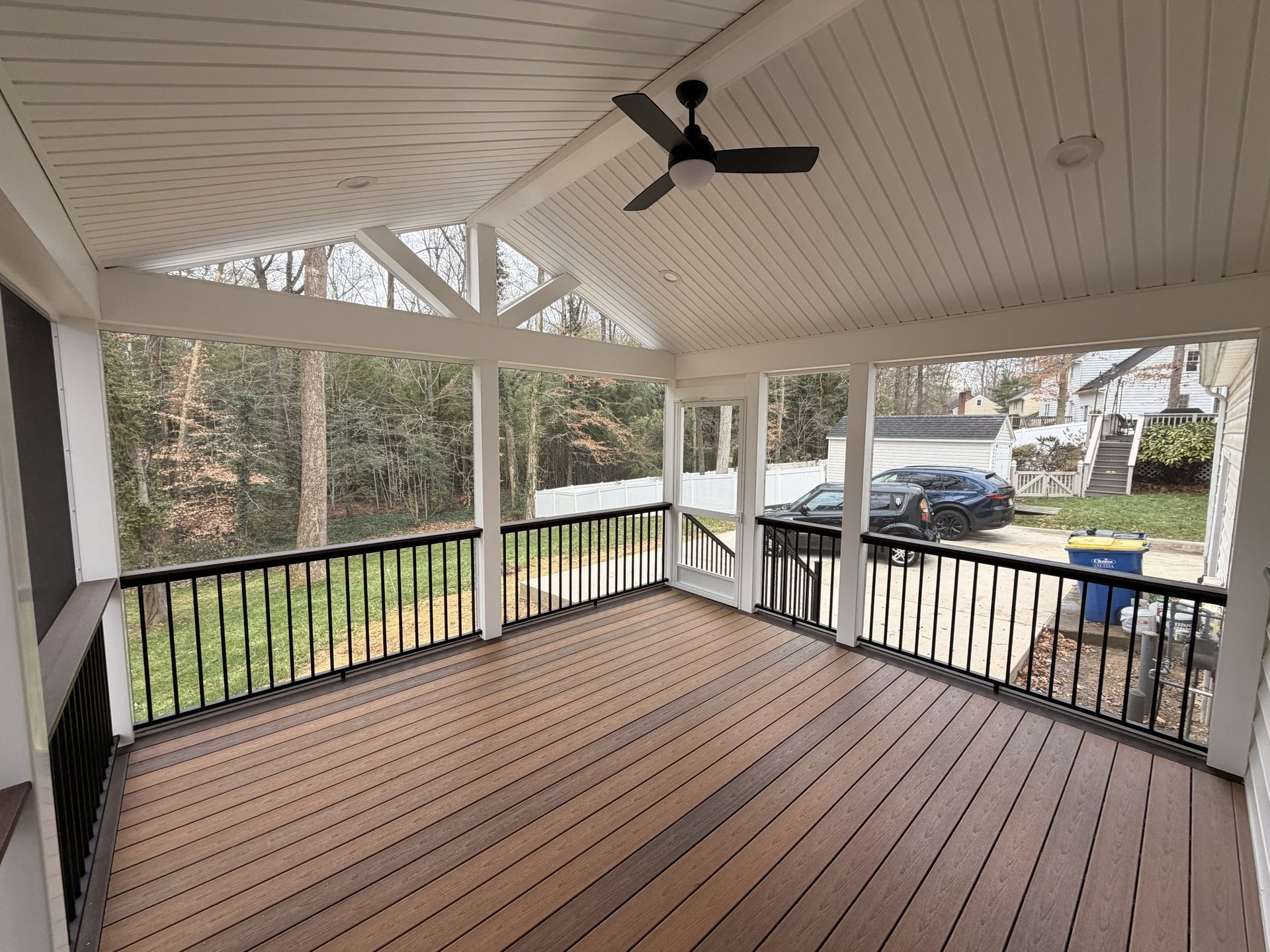 Covered screened porch with wood floor, white railing, ceiling fan, and a yard view beyond.