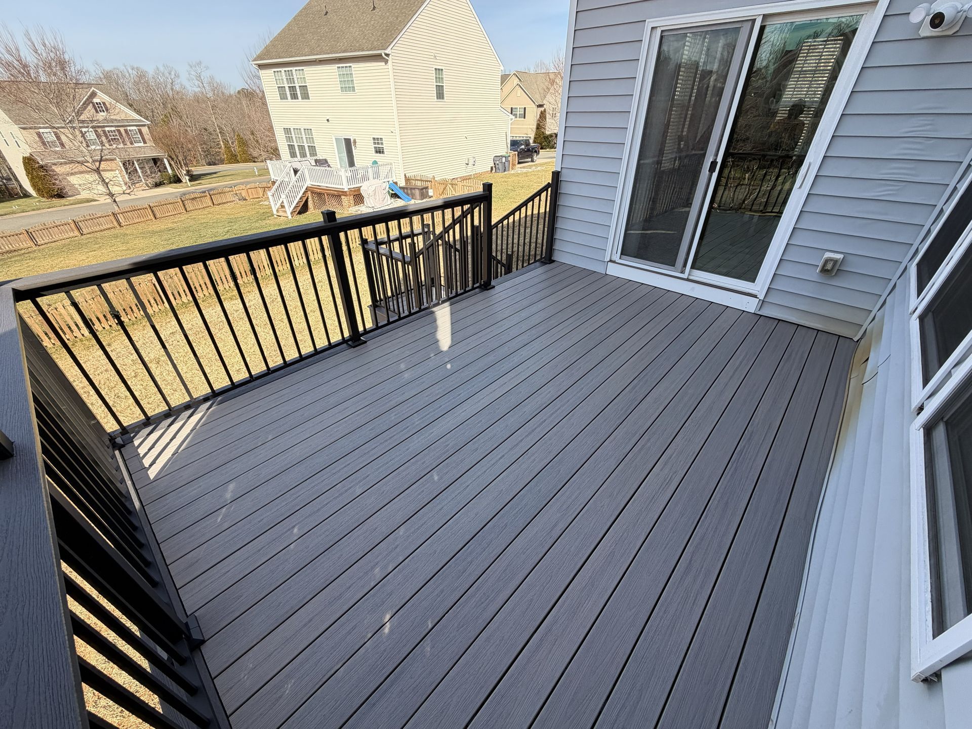 Back deck with gray composite flooring and black railing beside a house, overlooking a yard