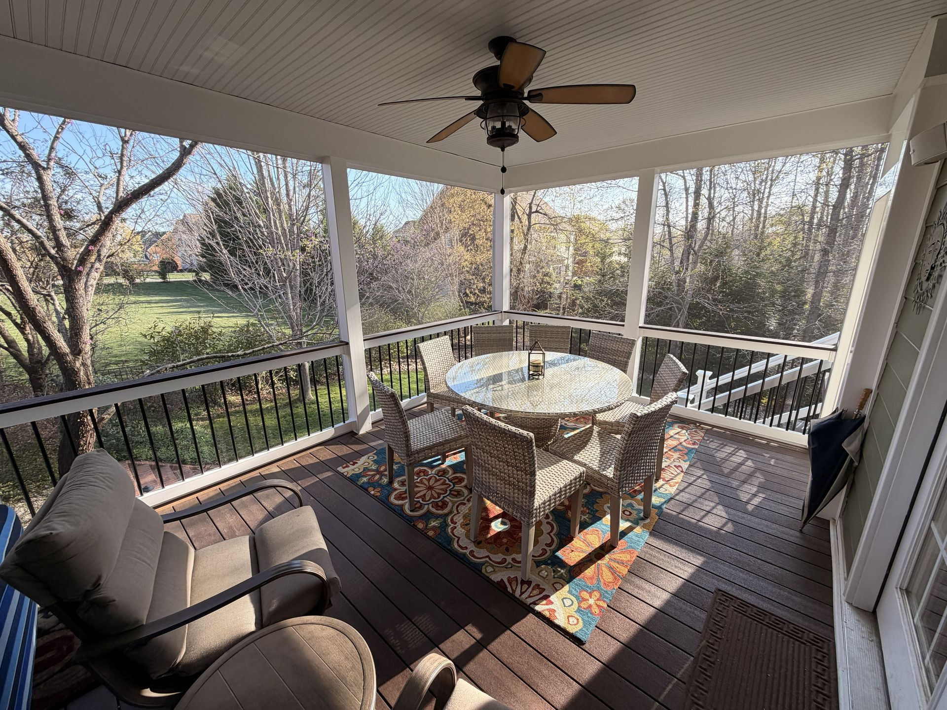 Covered porch with wicker dining table, cushioned chairs, and wooded backyard view