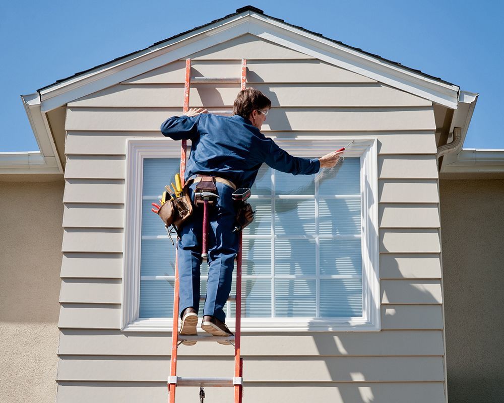 Worker on a ladder painting a house exterior beneath a gable roof