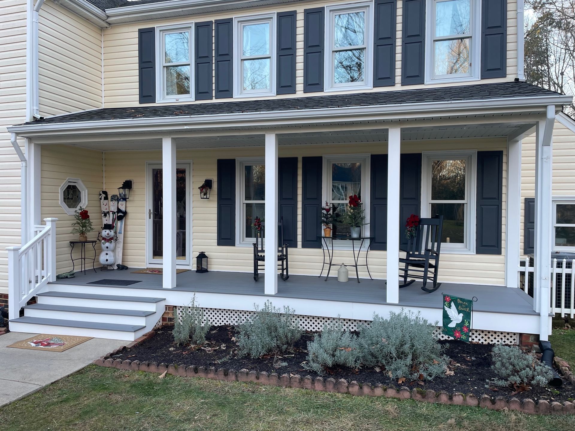 Front porch of a beige house with white columns, black shutters, steps, and seasonal Halloween decorations.