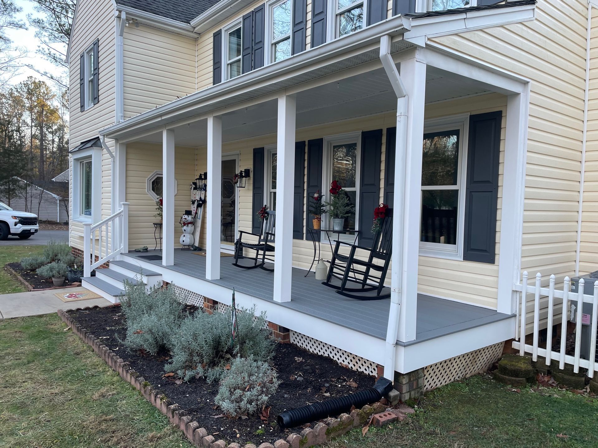 Front porch of a beige house with white columns, rocking chairs, and black shutters