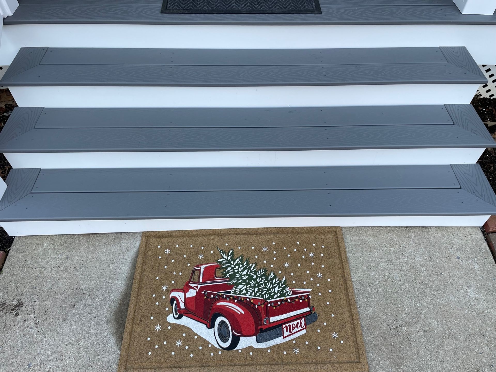 Red vintage truck decoration on a doormat beside gray front steps and a garage door