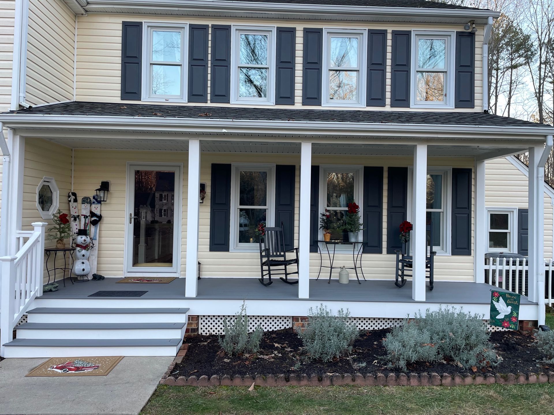Front porch of a beige two-story house with white trim, dark shutters, and autumn decorations