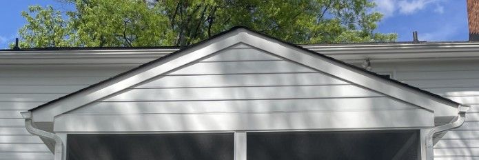 White house gable with two dark windows, set against blue sky and green trees