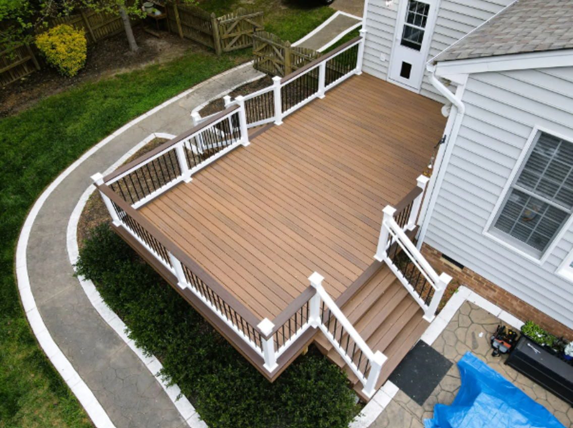 Wooden backyard deck with white railings and steps beside a house, viewed from above.