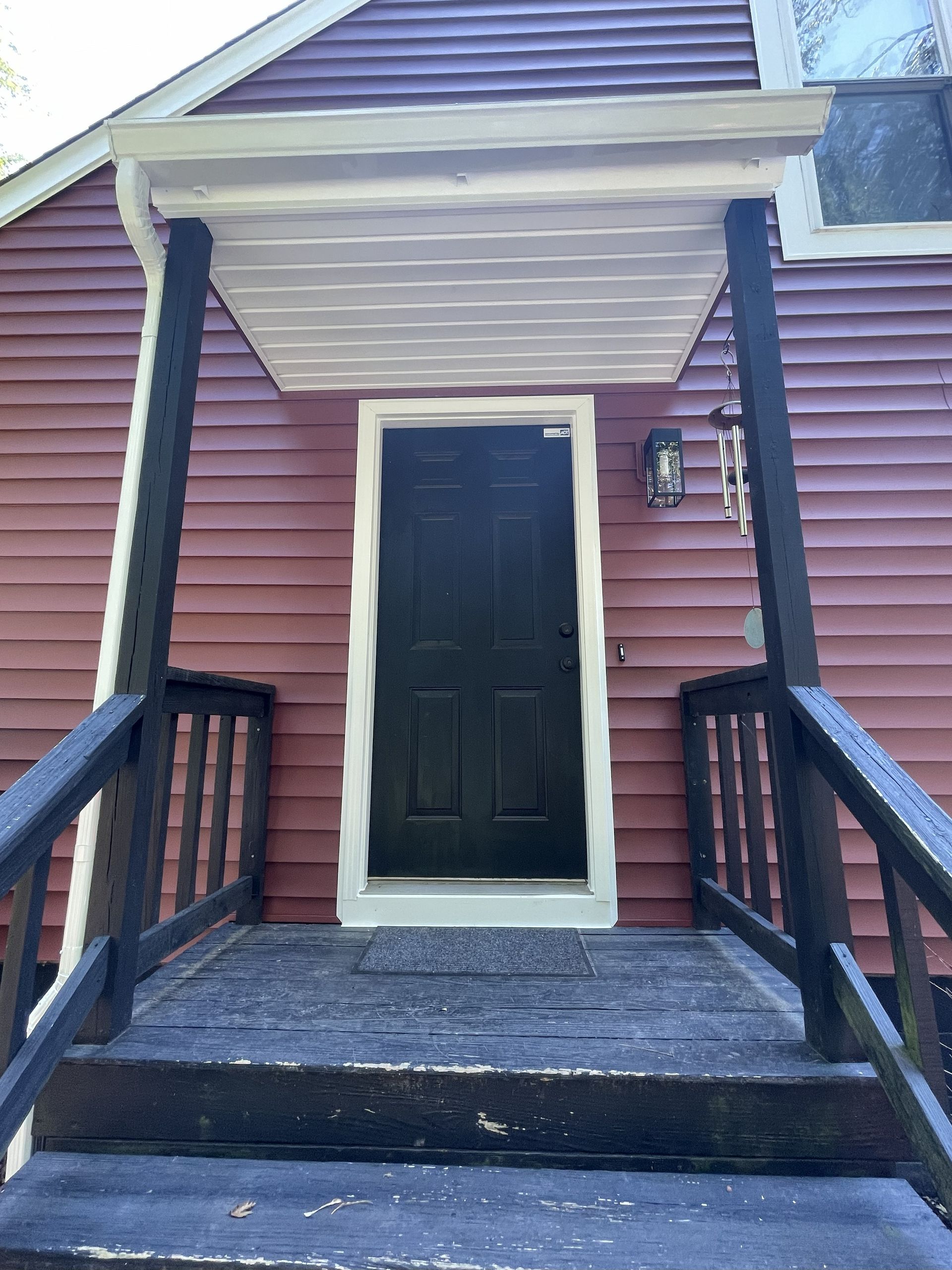 Front porch with black door, white trim, red siding, and wooden railings leading up steps.