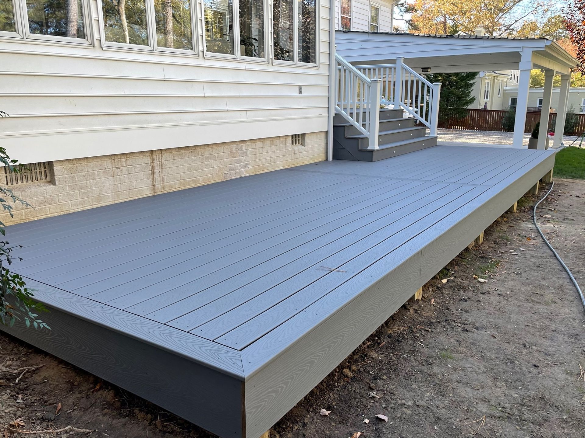 Gray raised deck beside a house with white railing and stairs