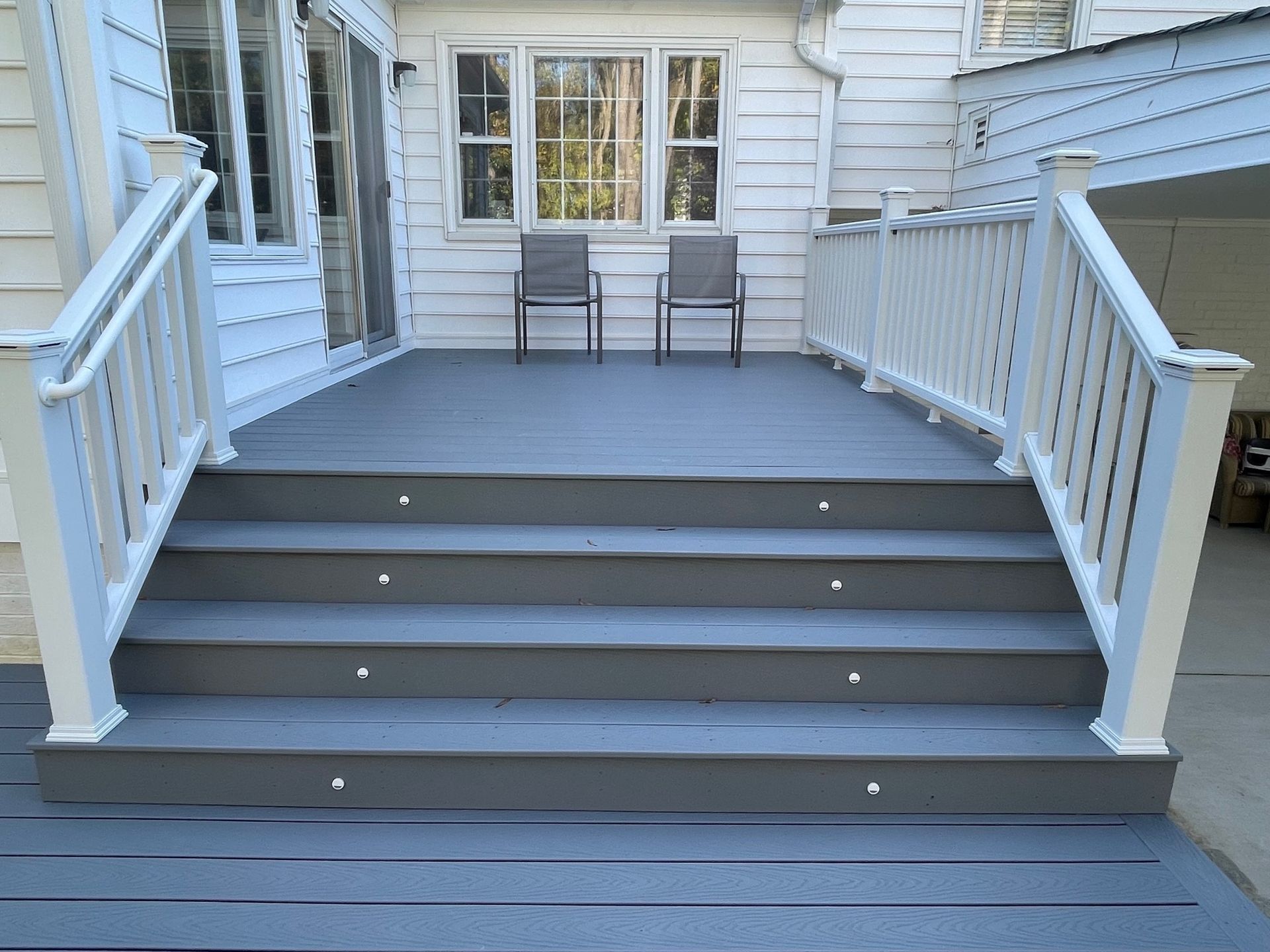 Front porch with gray steps, white railings, and two chairs by a window.