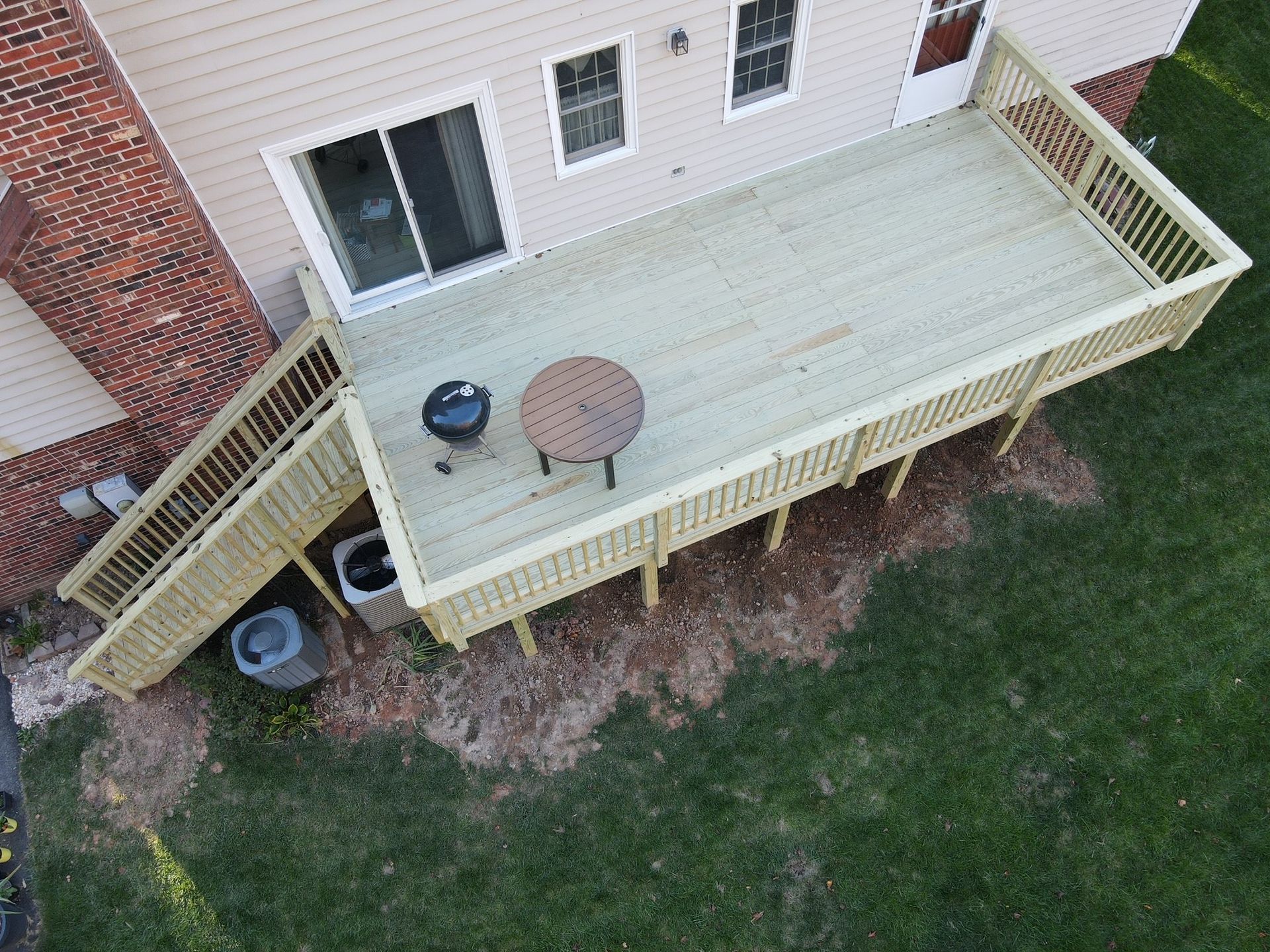 Backyard deck with a round table and grill beside a house, stairs leading to the lawn.