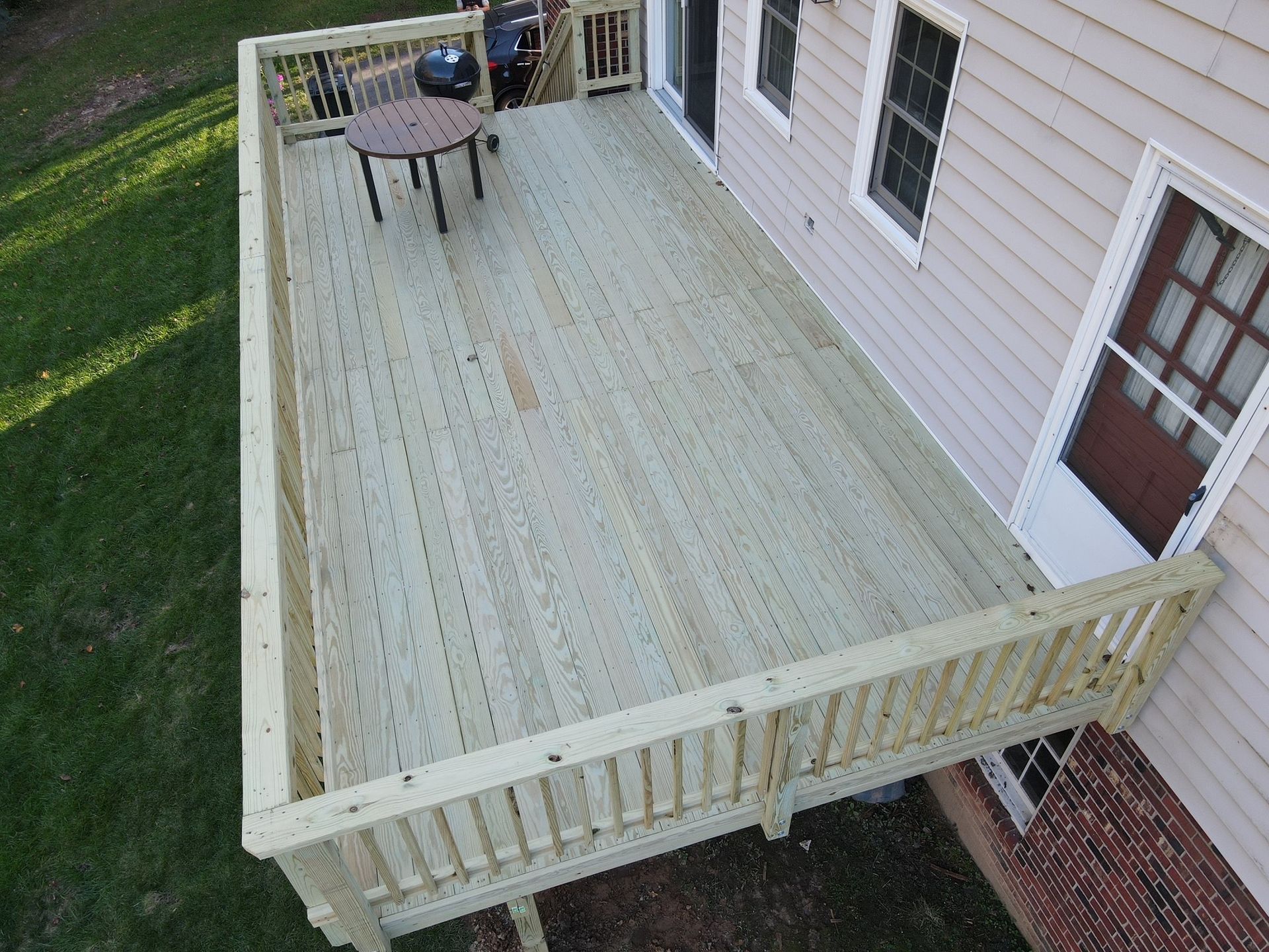 Wooden backyard deck beside a house, with a small table and grill near the far end.