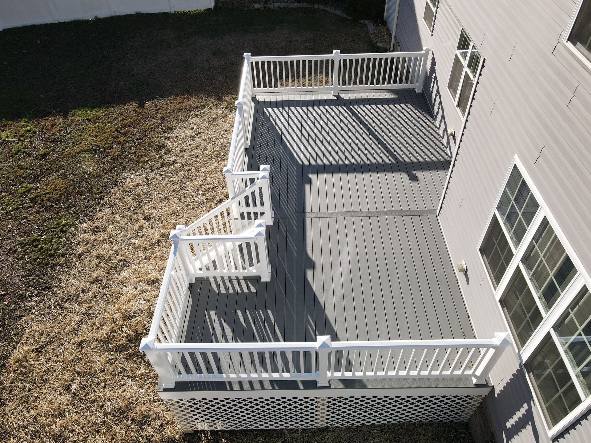 White wooden deck/patio beside a house, with railing, steps, and backyard gravel area.