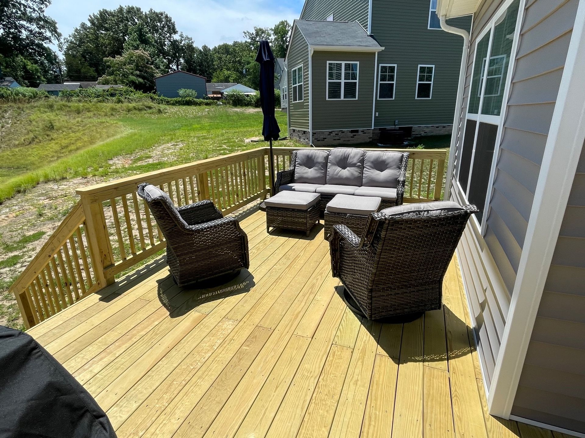 Back deck with wicker chairs and gray sofa on a wooden patio beside a house and grassy yard.