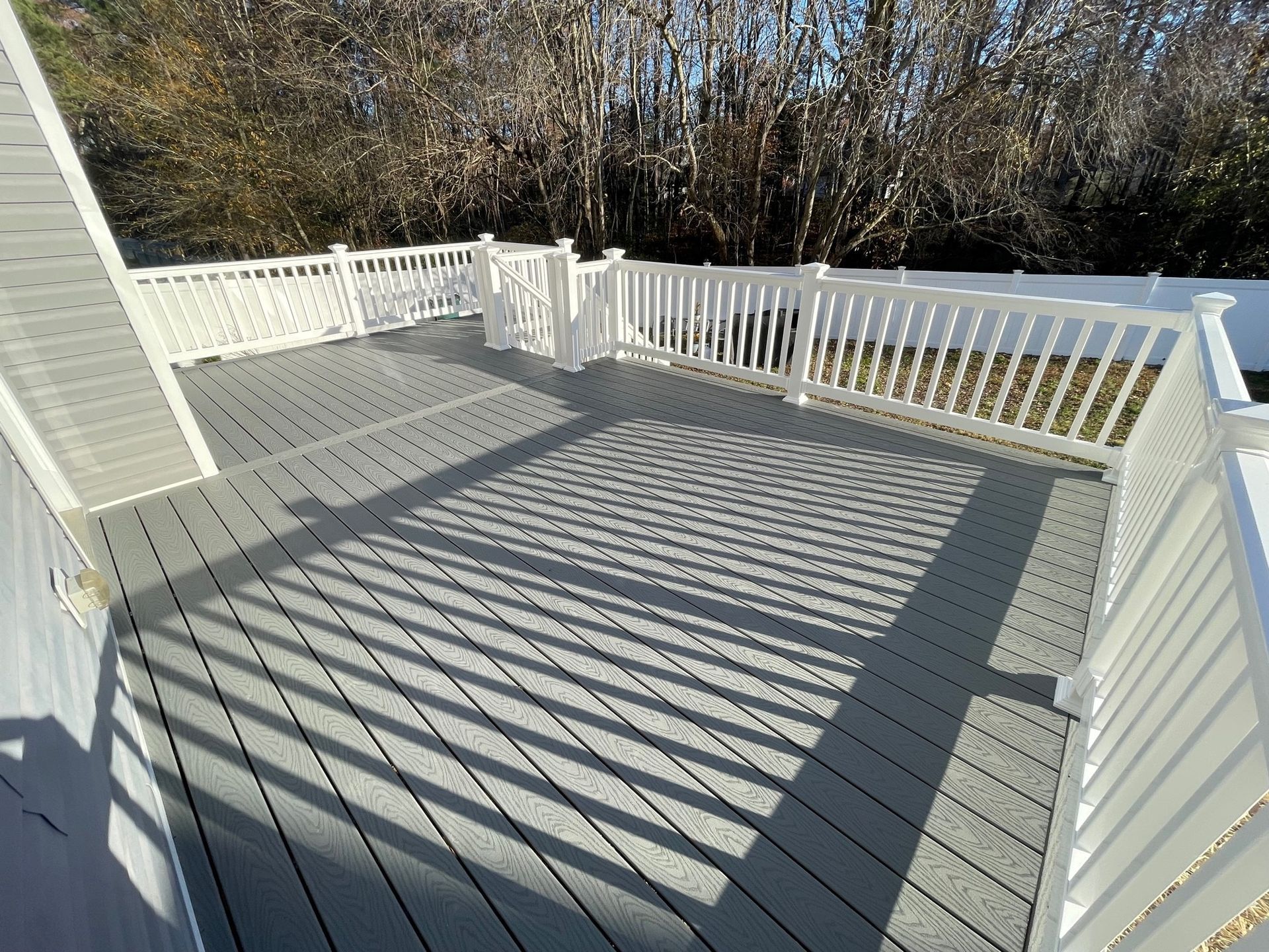 White backyard deck with railings and long fence shadows in bright sunlight