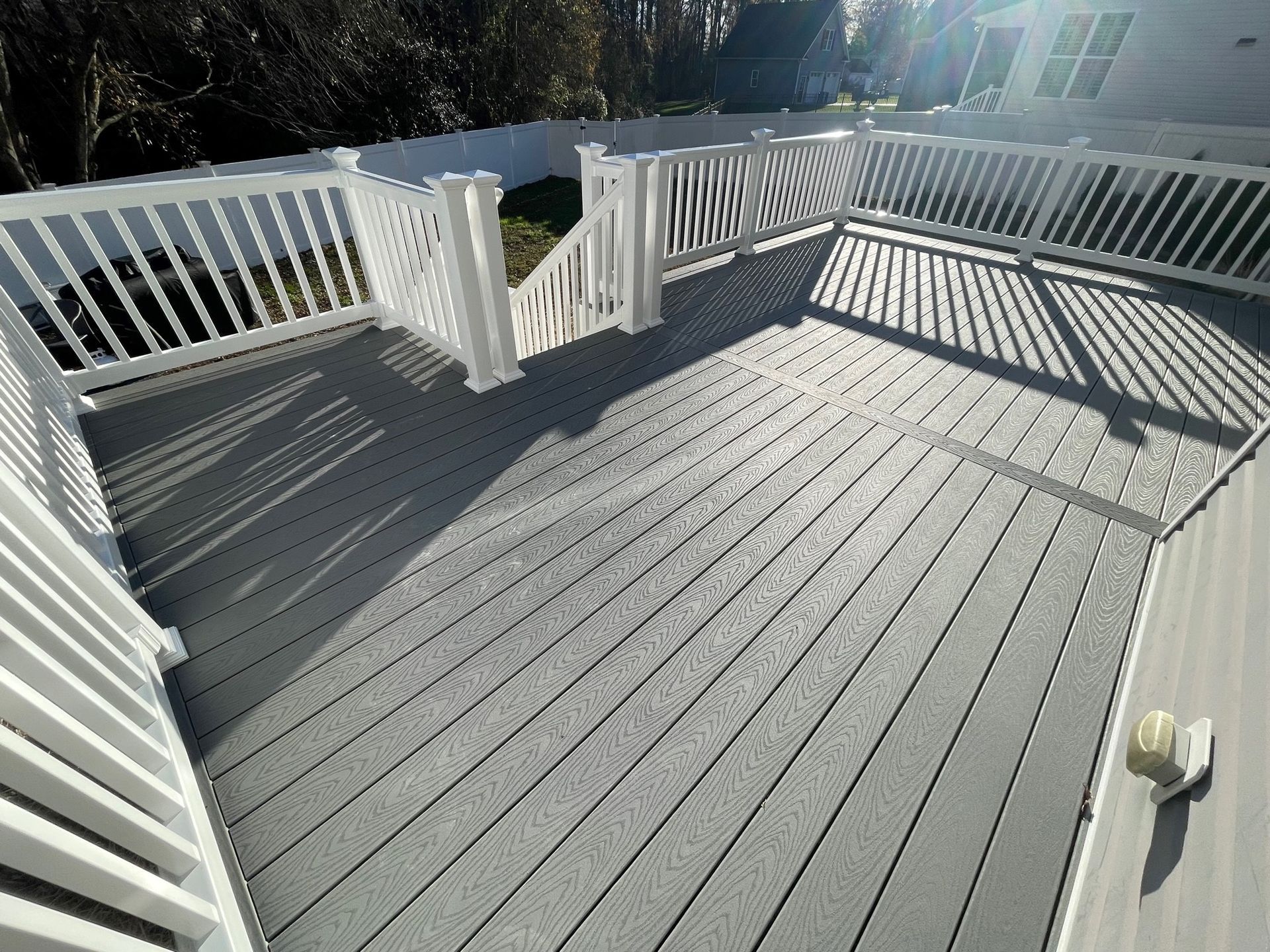 Sunlit gray deck with white railings and long shadows from the porch