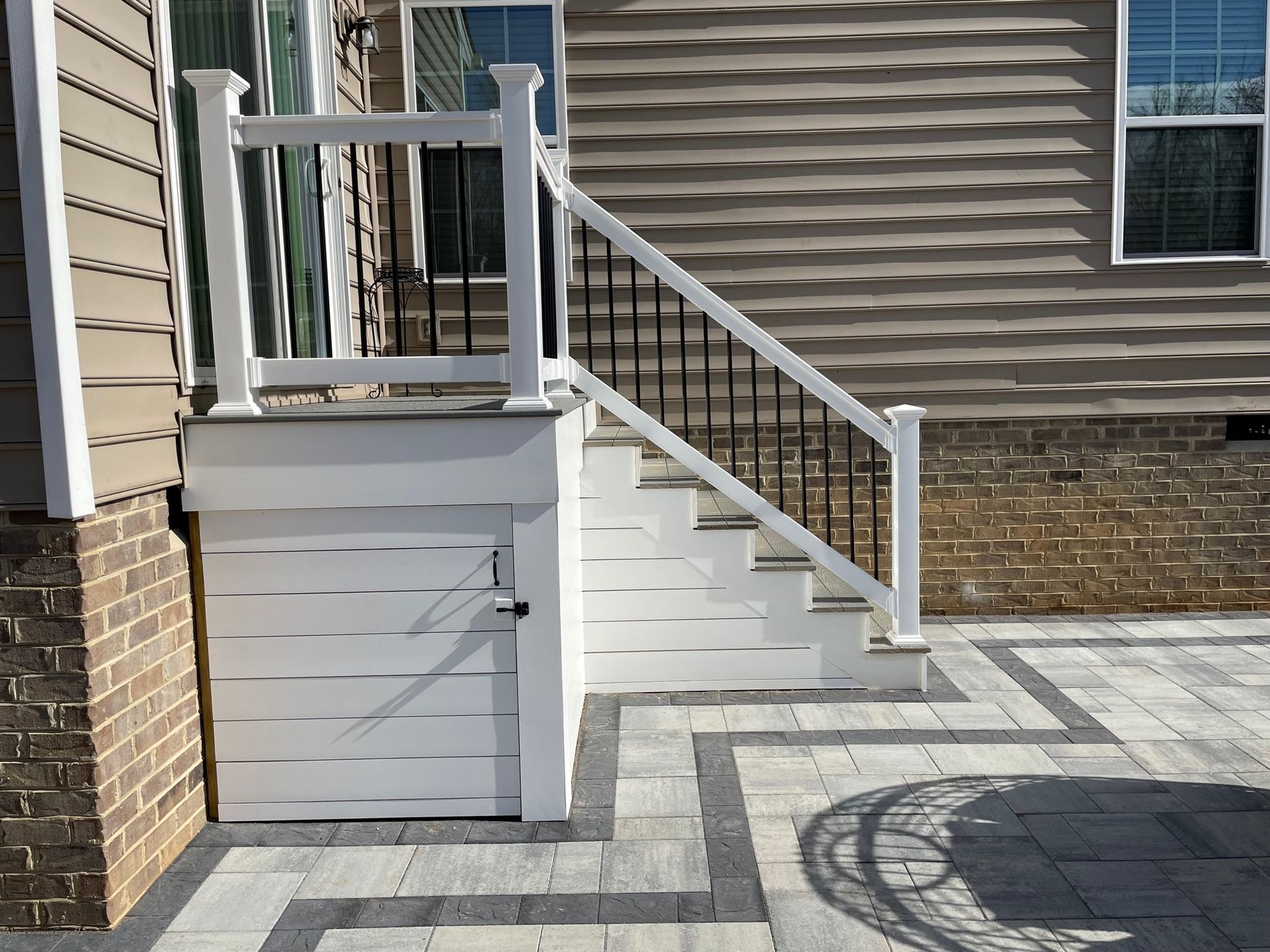 Outdoor concrete ramp and stairs with white railings beside a house entrance