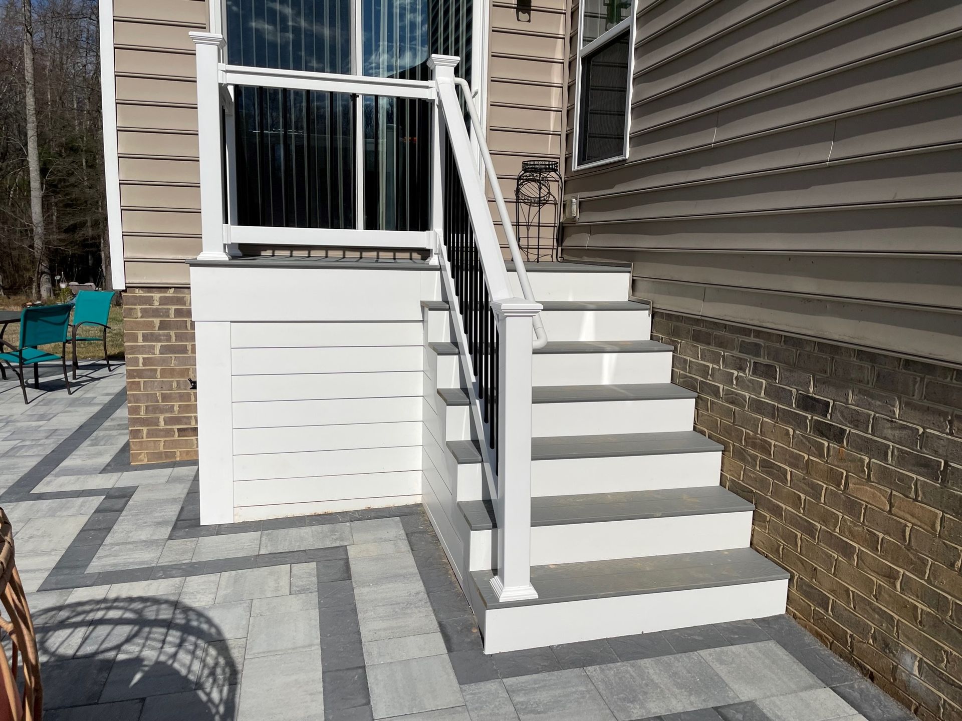 White exterior staircase with railings leading to a raised porch beside a brick house