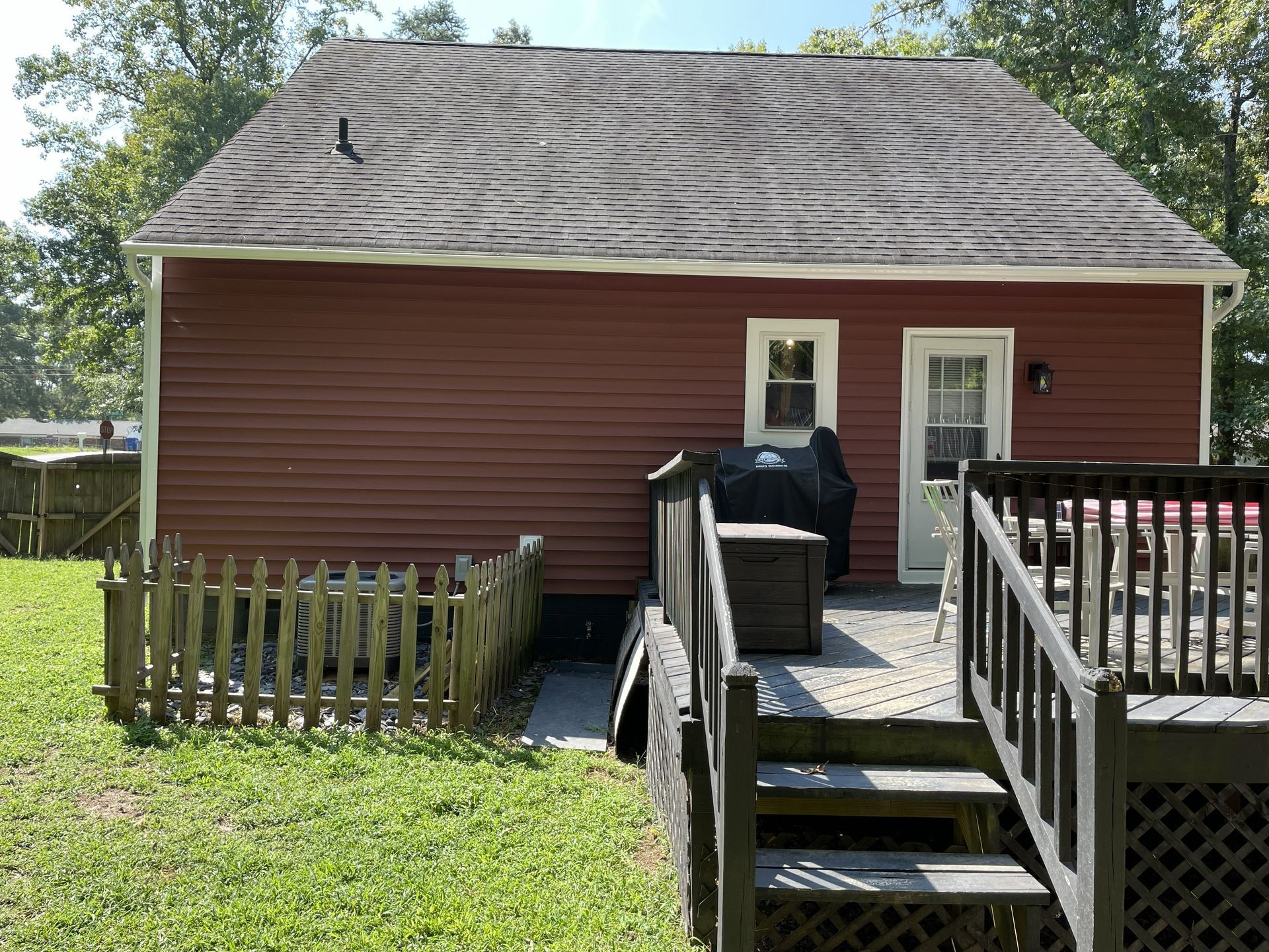 Red house with deck stairs, small fence, and two white doors under a cloudy sky.