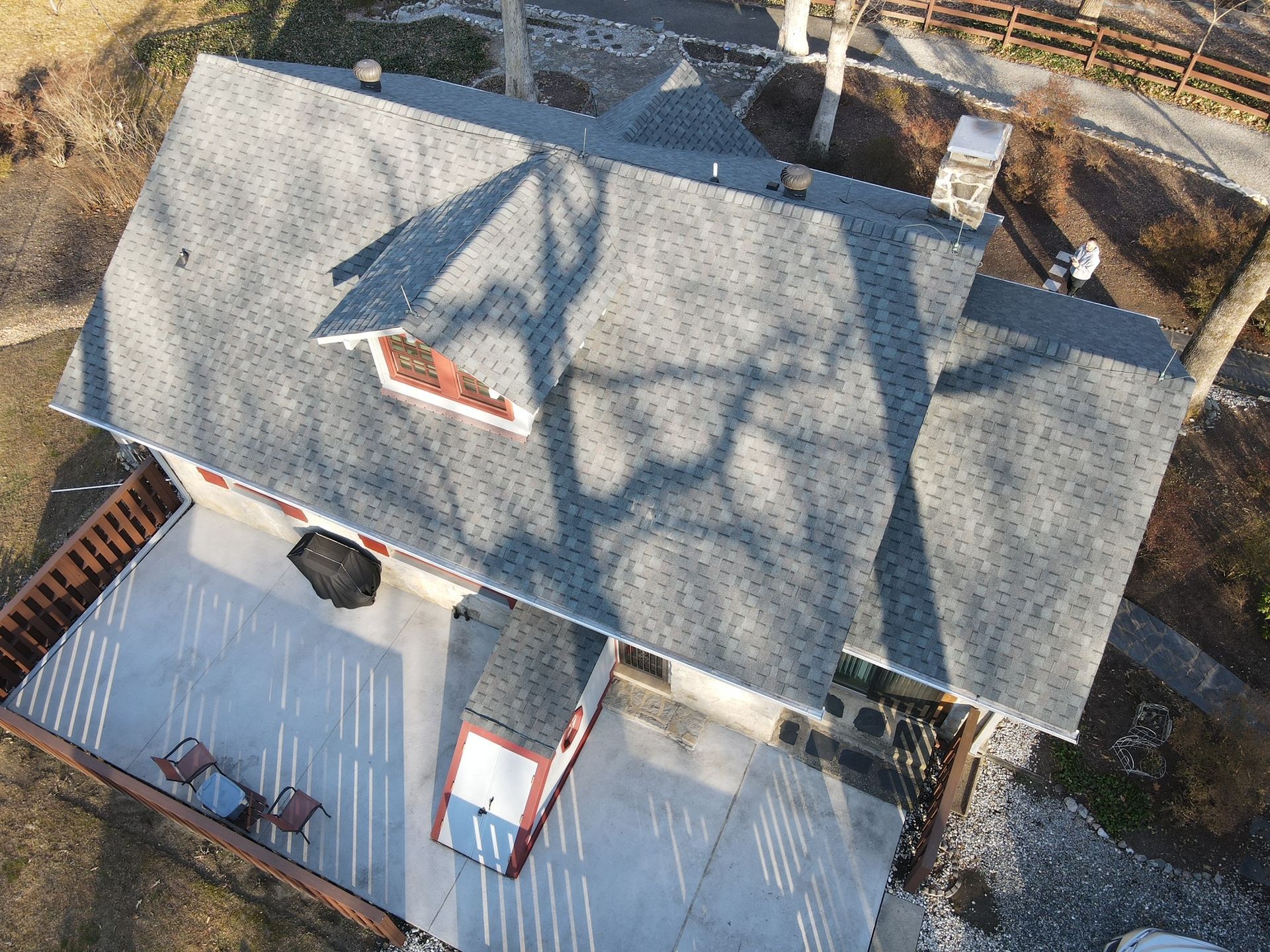 Aerial view of a gray-roofed house with a covered porch and wooden deck, casting long shadows.