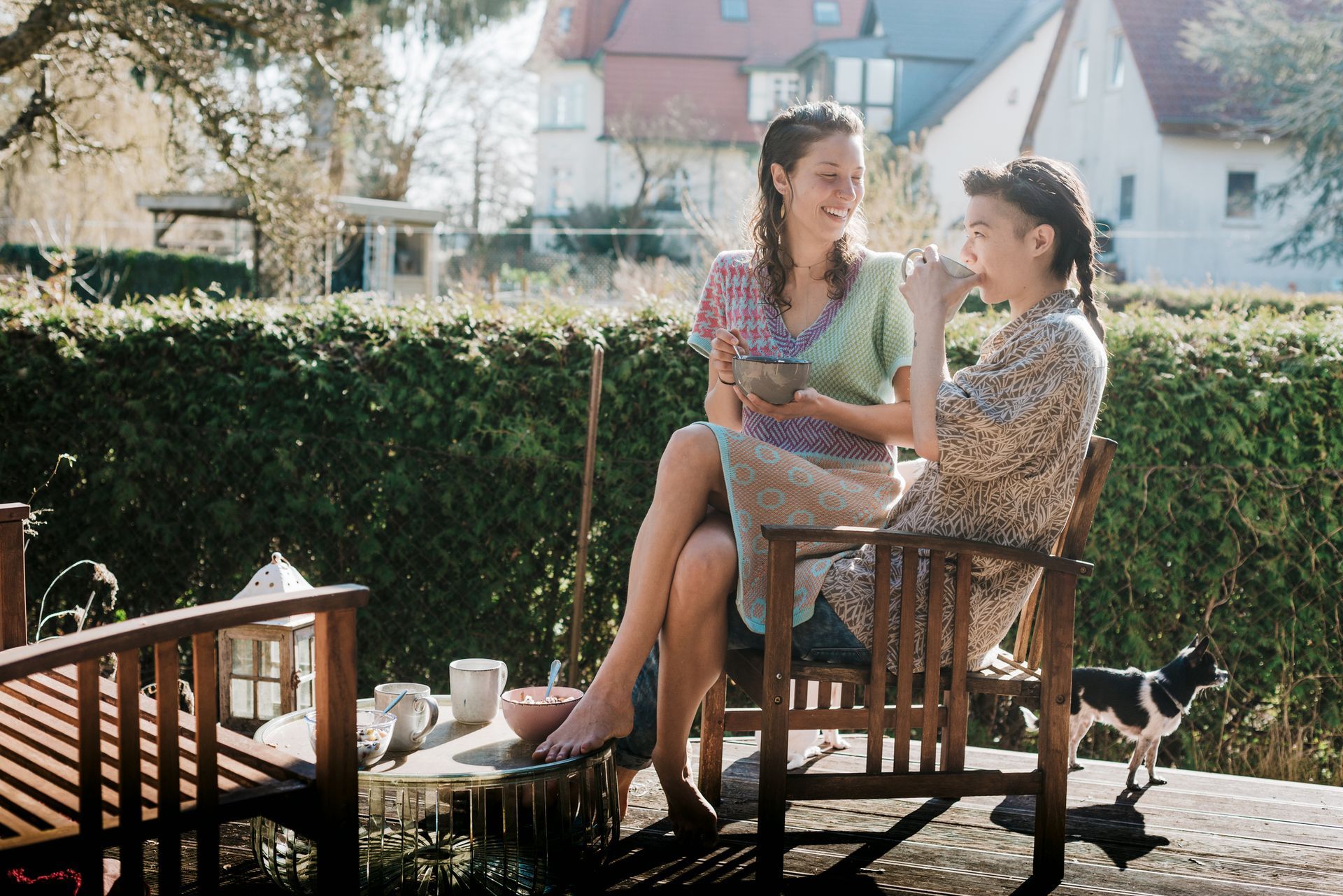Two people share food on a sunny deck with a small dog nearby. Two people share food on a sunny deck with a small dog nearby.