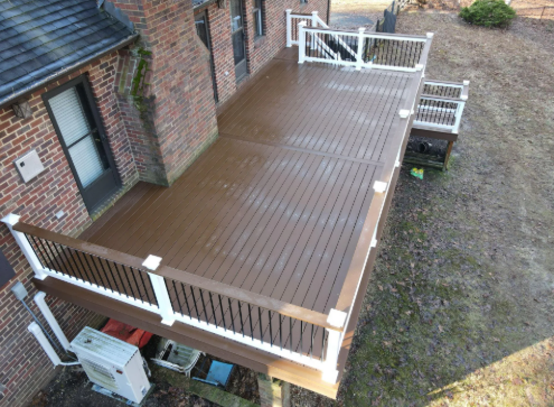 Raised brown composite deck with white vinyl railings, black balusters, post caps, and staircase.