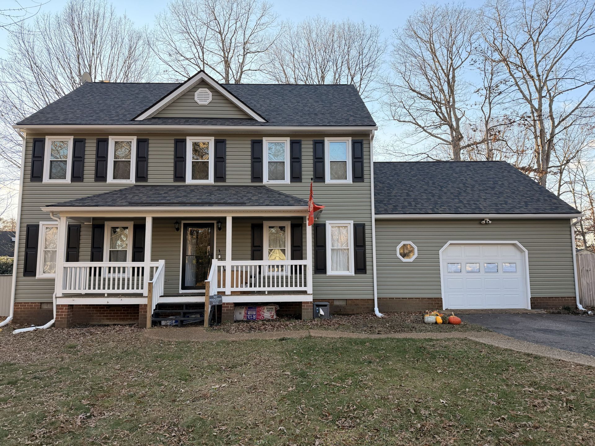 Two-story gray house with white trim, front porch, garage, and leafless trees in the yard