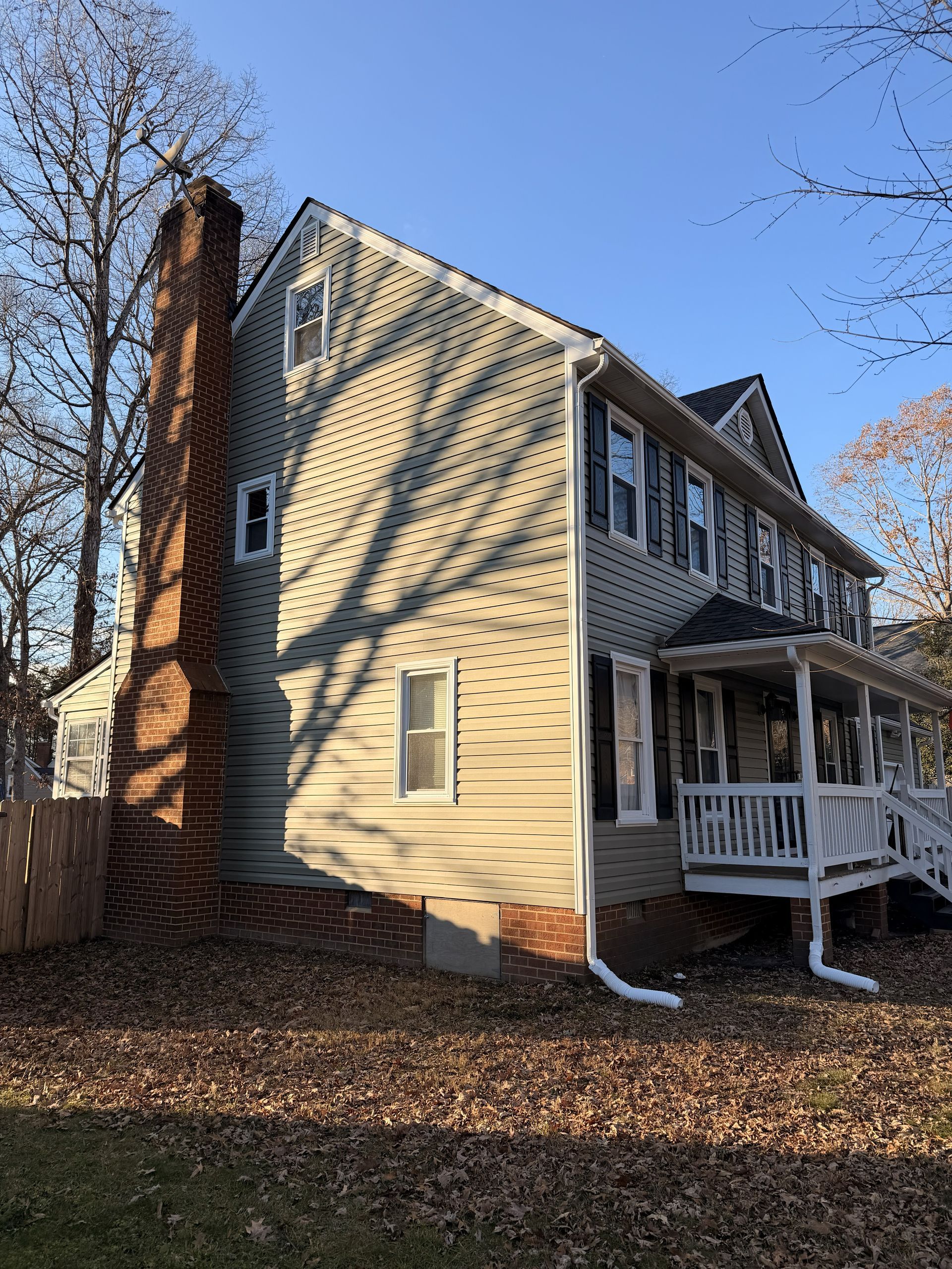 Sunlit beige house with brick chimney, porch, and leaf-covered yard in autumn