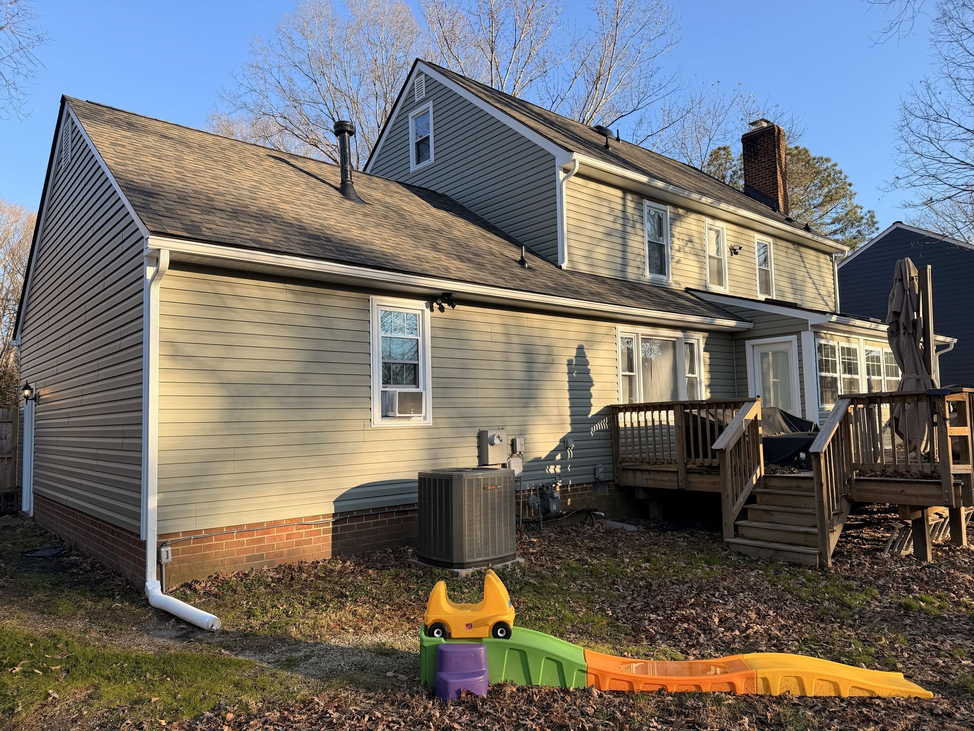 Suburban house with beige siding, deck, and orange safety barrier in the yard