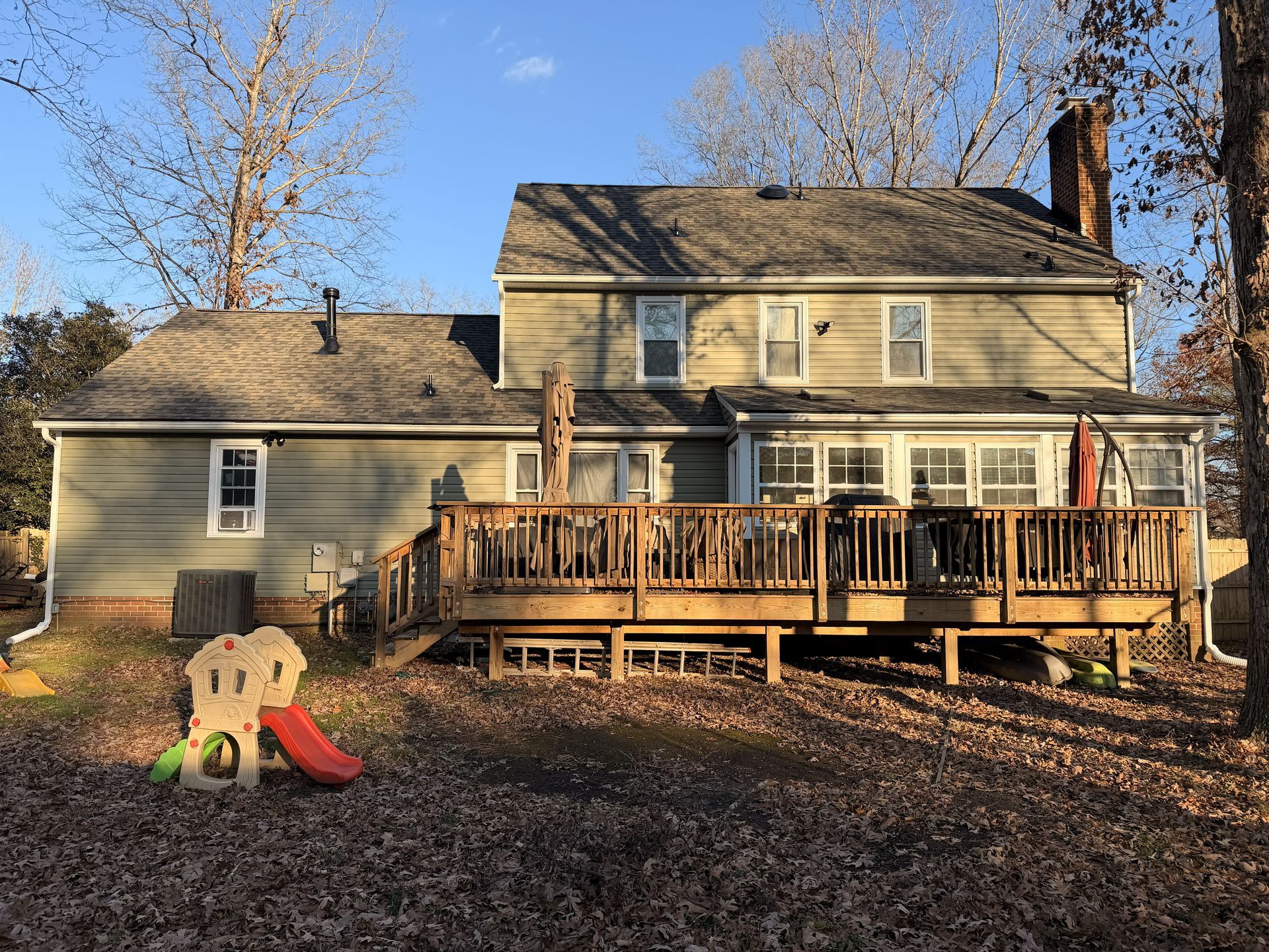 Two-story house with a wooden deck and a small playhouse in a leaf-covered backyard