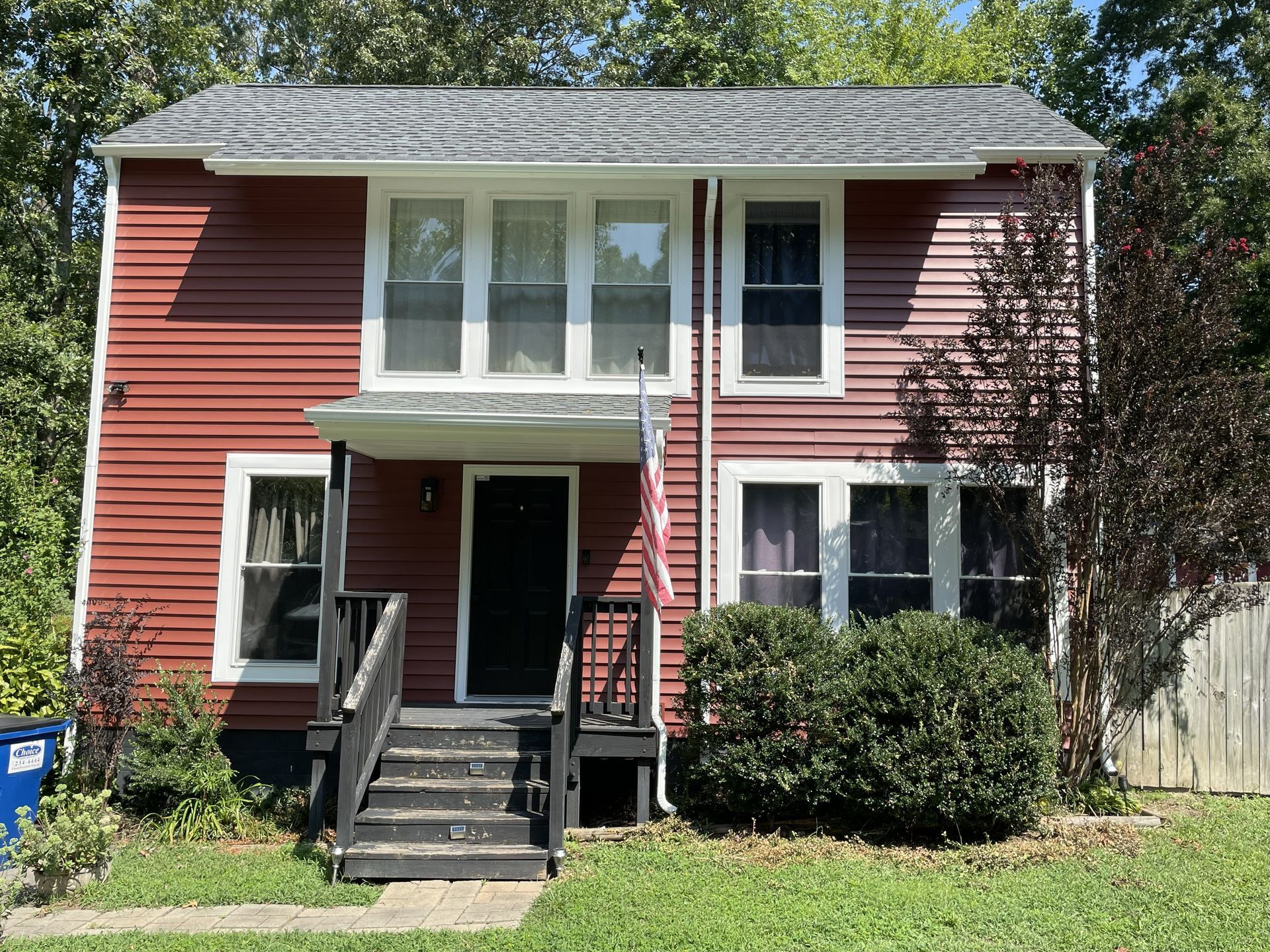 Red two-story house with white trim, front steps, and shrubs in the yard