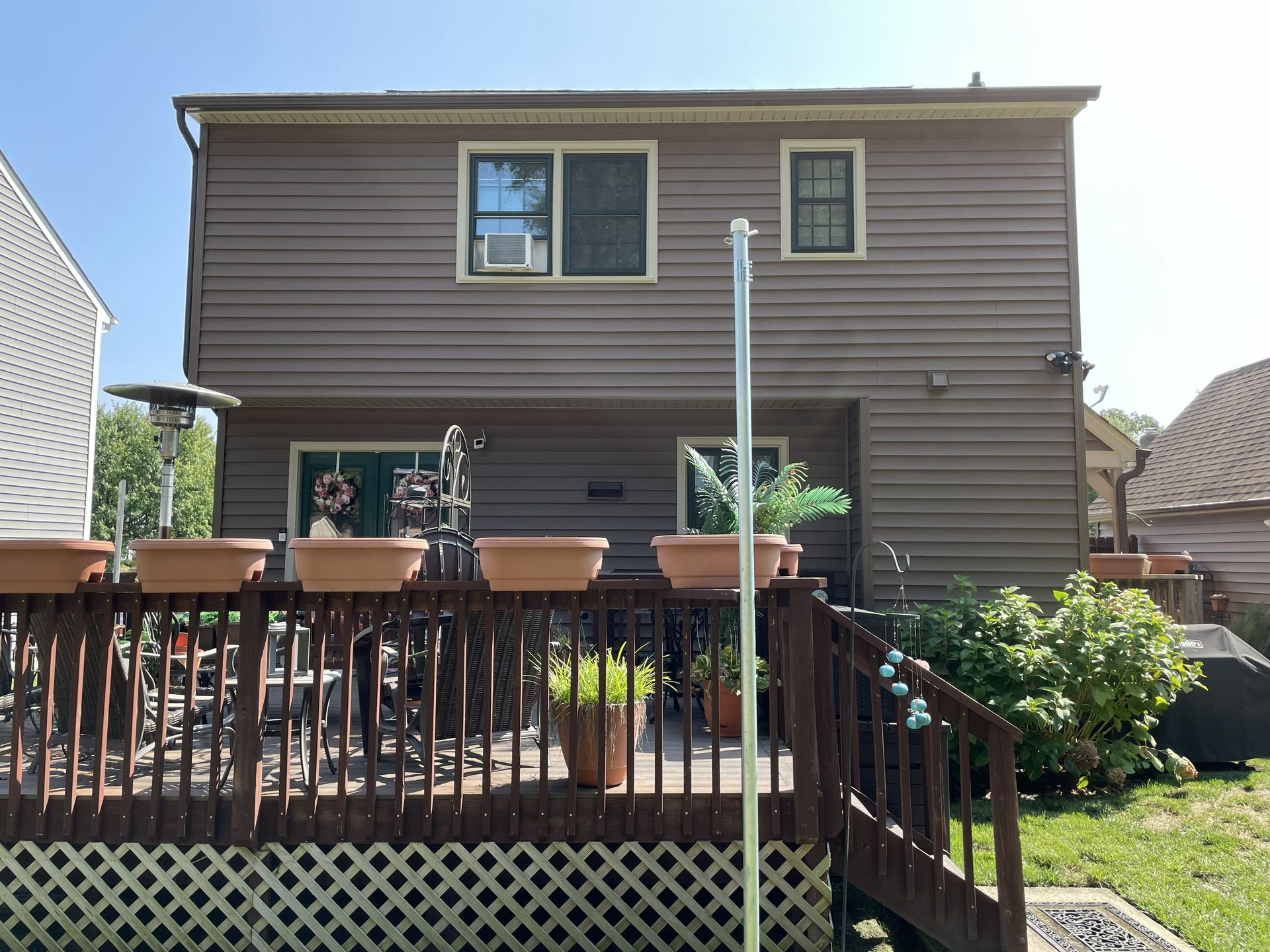 Backyard deck and brown two-story house with outdoor furniture and patio plants