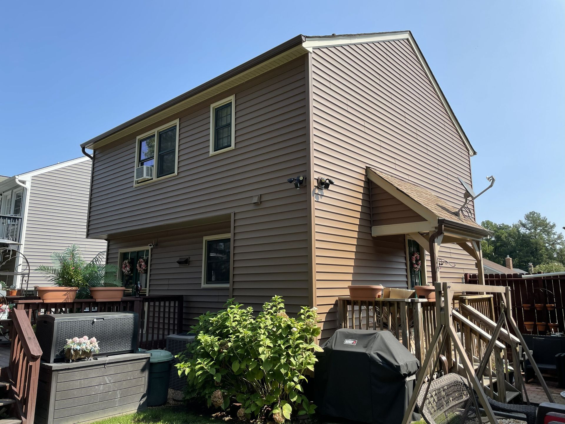 Tan-sided two-story house with a small porch and fenced backyard on a sunny day