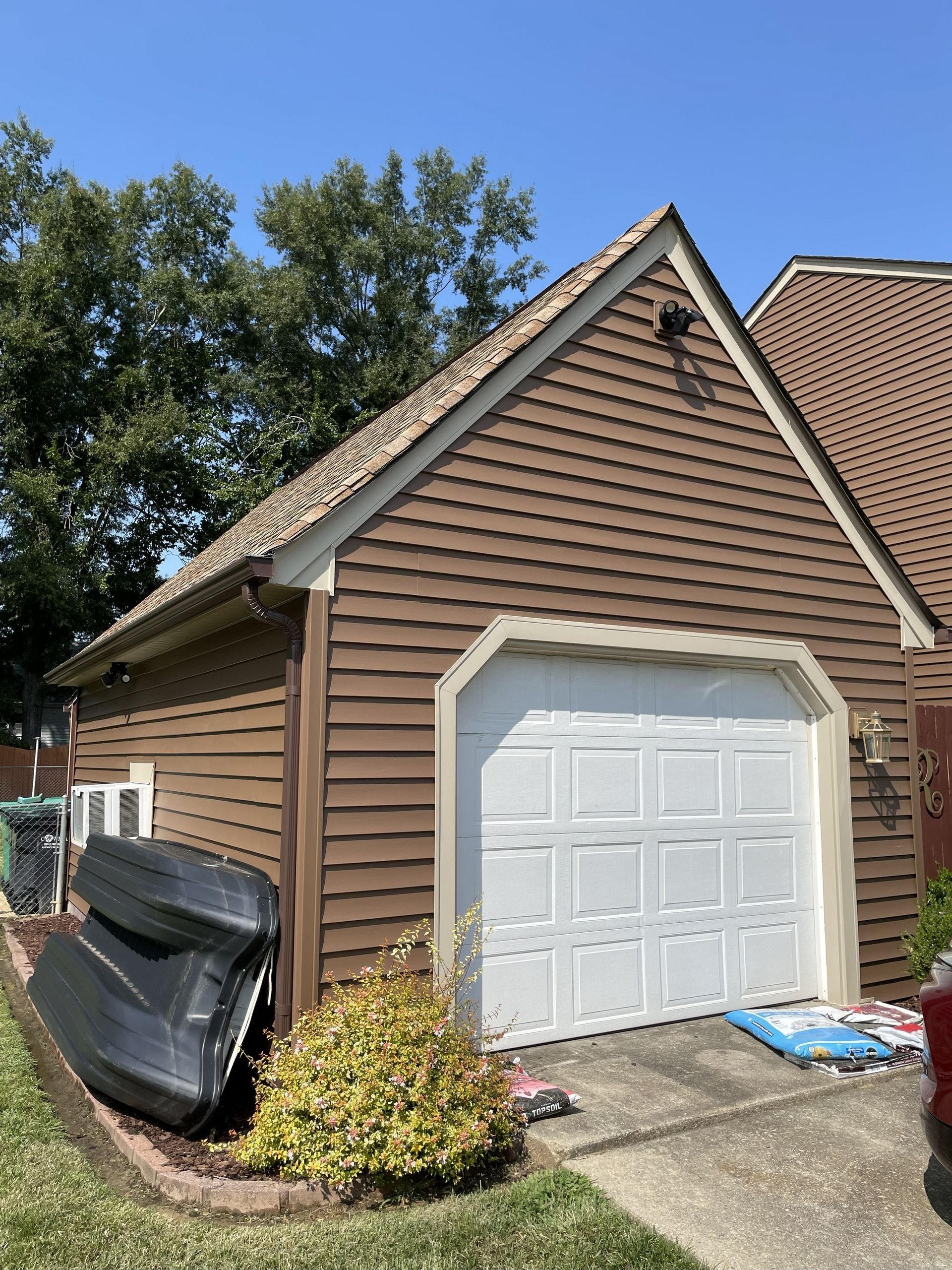 Detached brown garage with white door and driveway, with a covered object along the side.