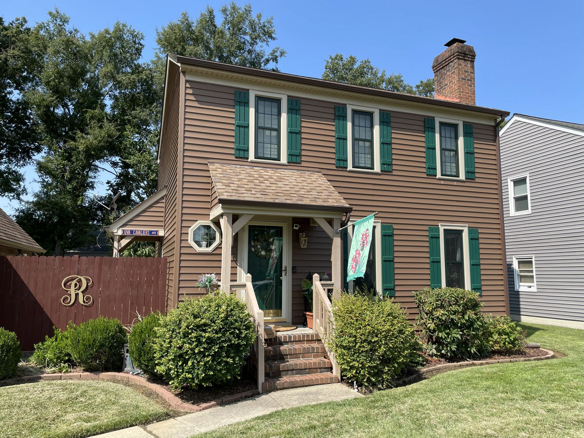Two-story brick house with green shutters and a front porch on a sunny suburban street