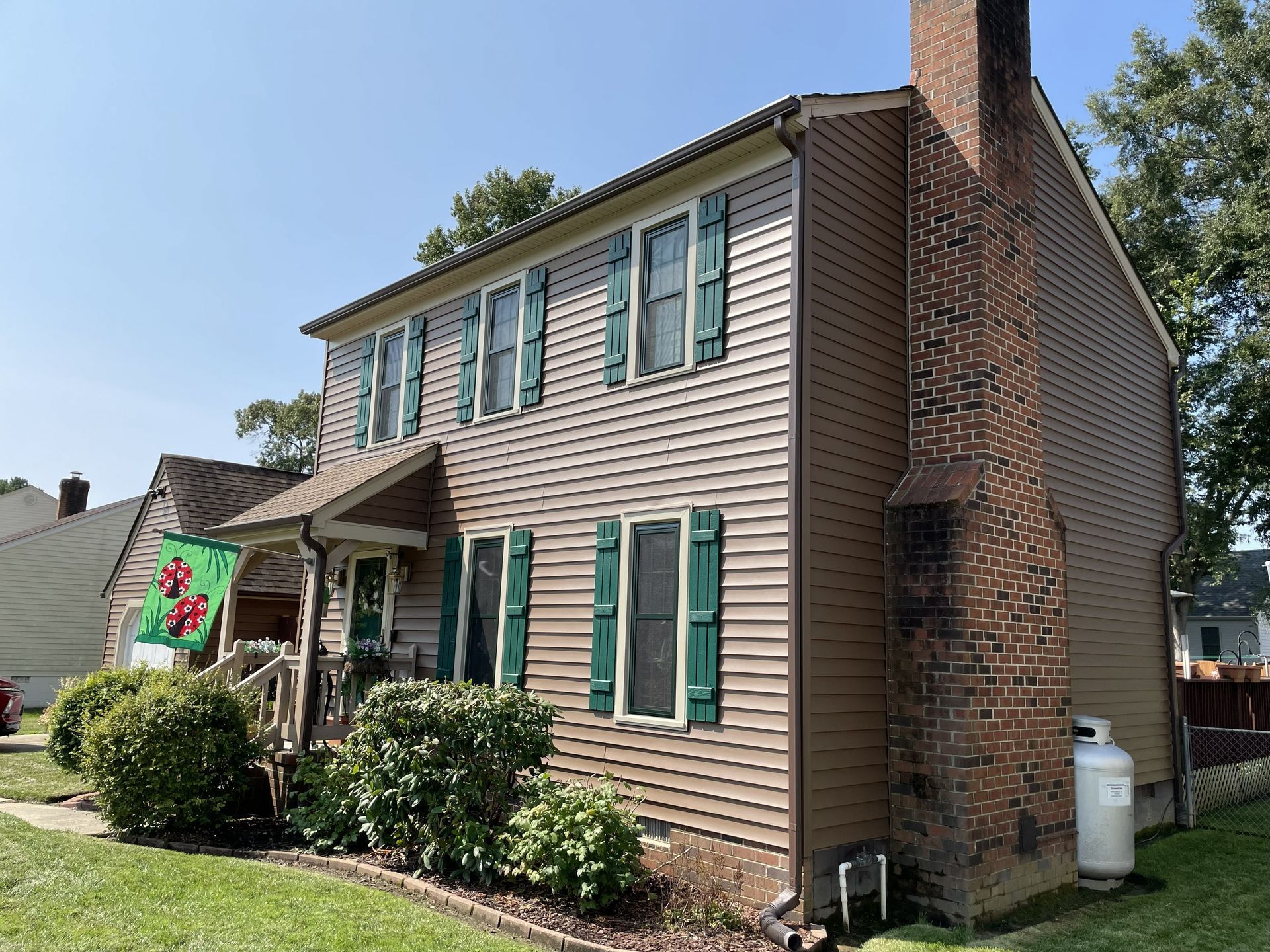 Two-story brick house with tan siding, green shutters, and a small front porch