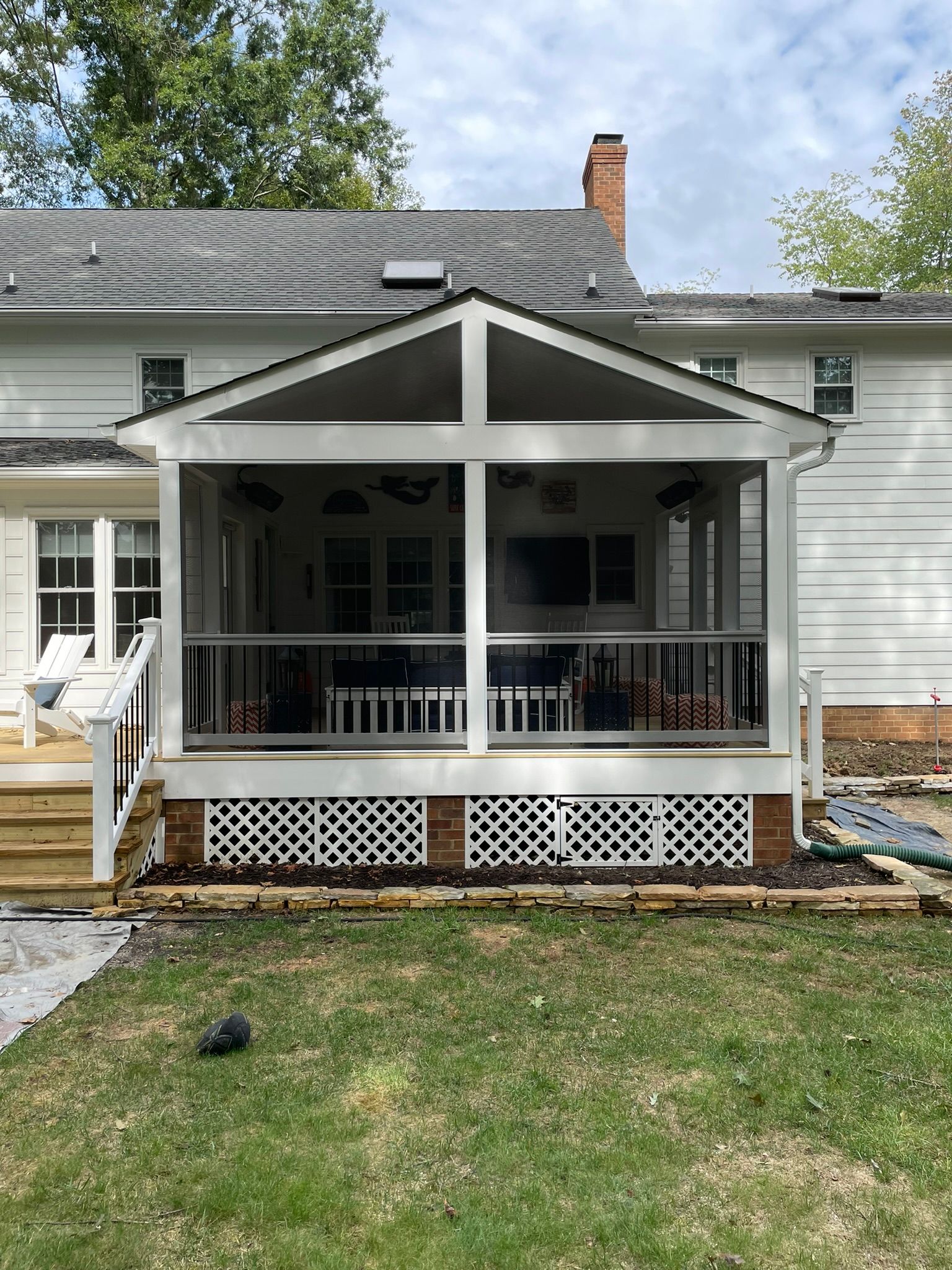 Back porch with white railings and lattice skirting on a light gray house, viewed from the yard.