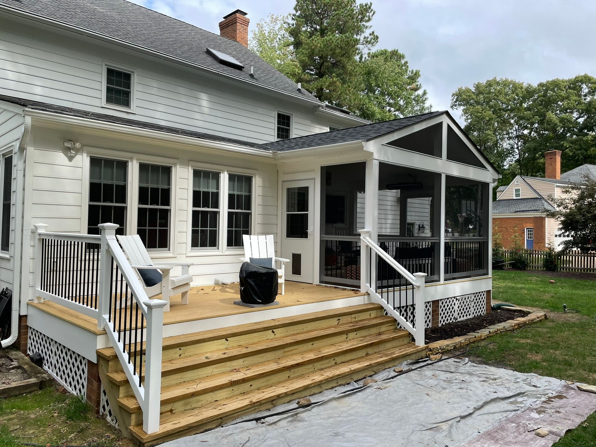 White house with a wooden back deck, steps, and screened porch in a leafy yard.