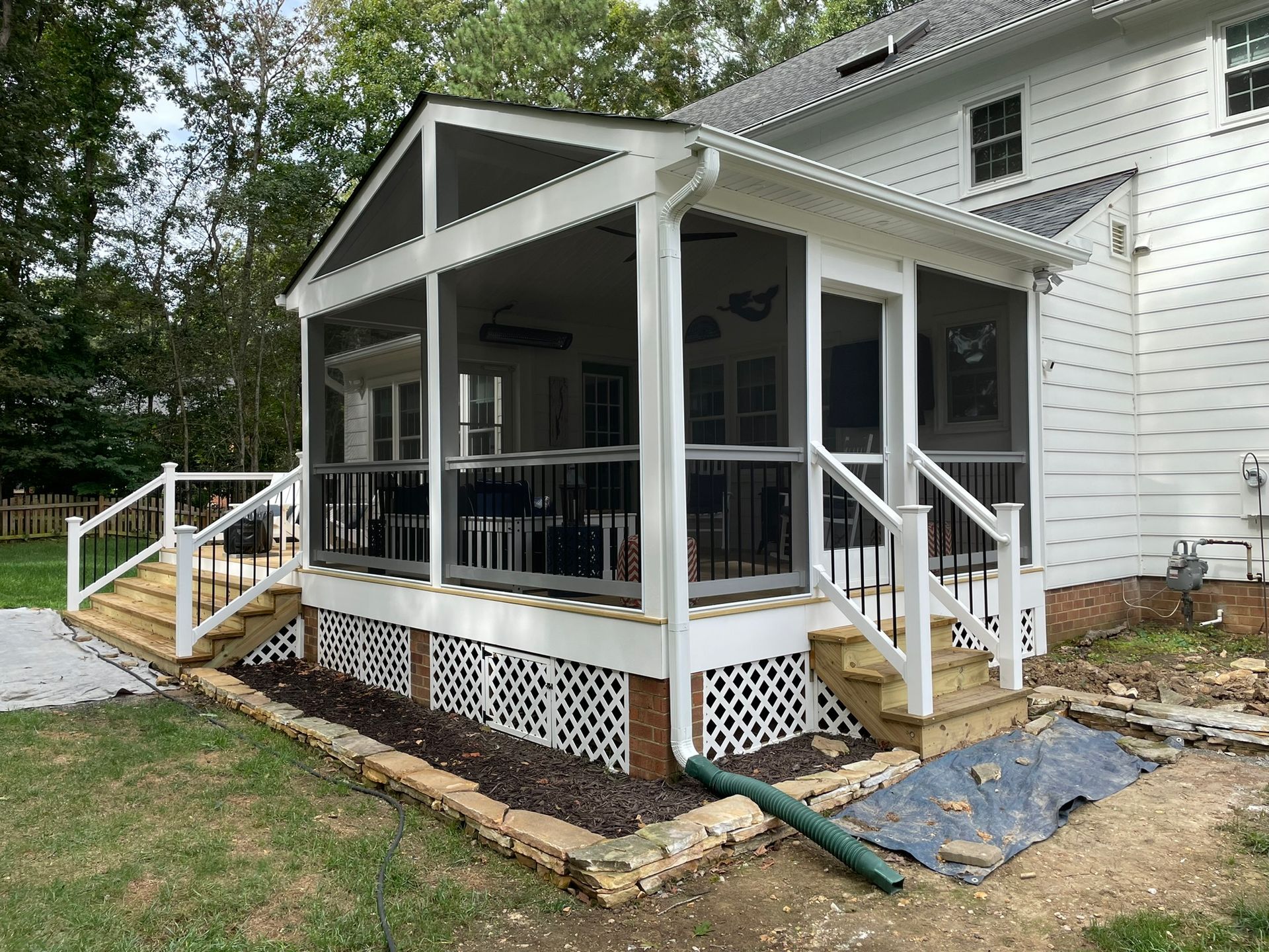 White screened porch addition on a house with steps and lattice trim, viewed from the yard
