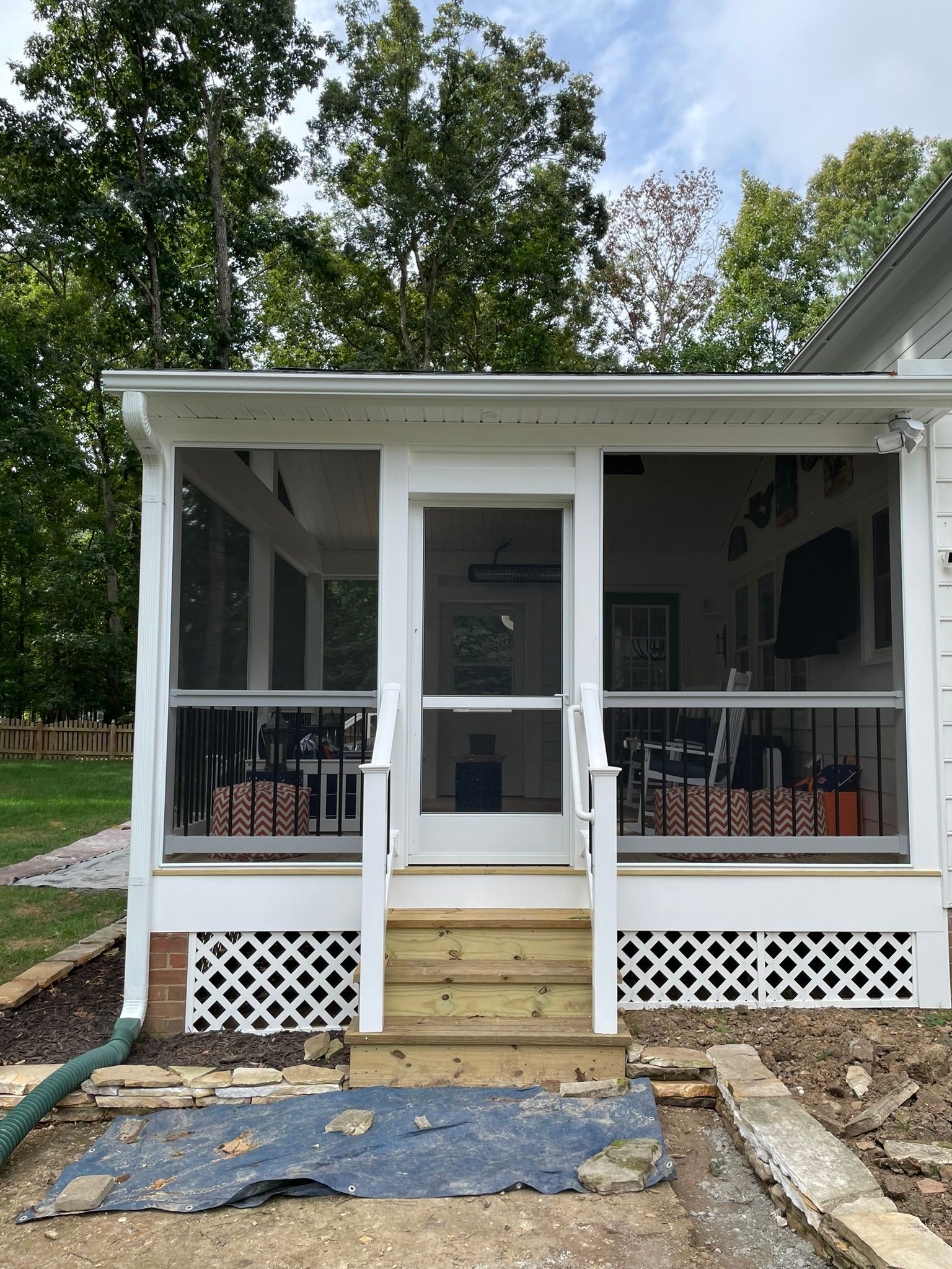 Front porch with white railing, central door, steps, and lattice skirting on a house surrounded by trees