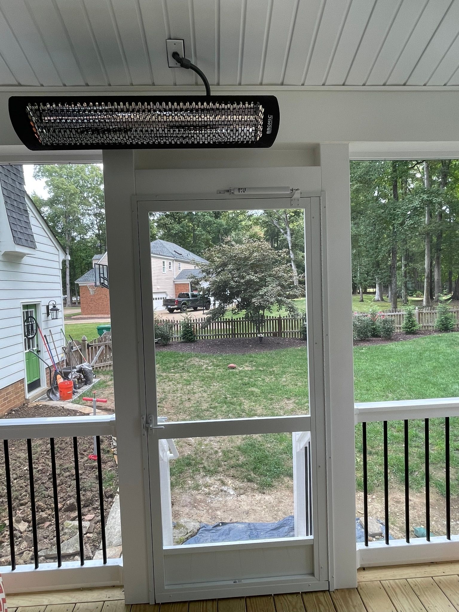 Covered porch with white railing and glass door, overlooking a grassy yard and trees.