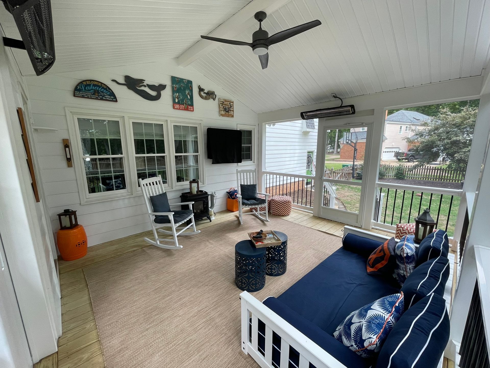 Screened porch with white chairs, navy daybed, ceiling fan, and lake view through open railing.