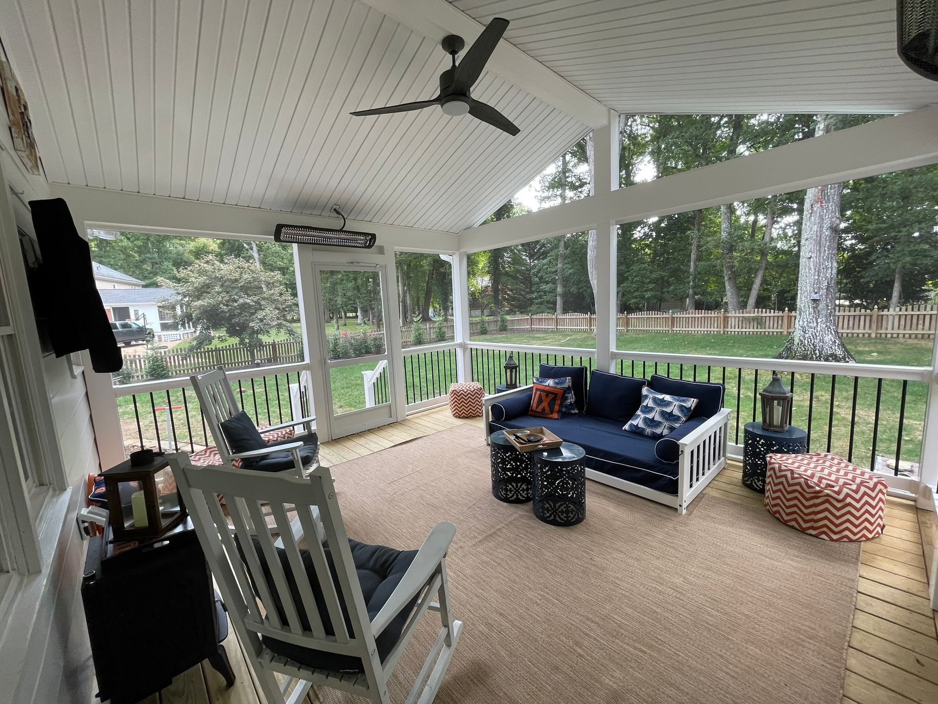 Porch seating area with white rocking chair, blue sofa, patterned ottoman, and view of yard through screened walls