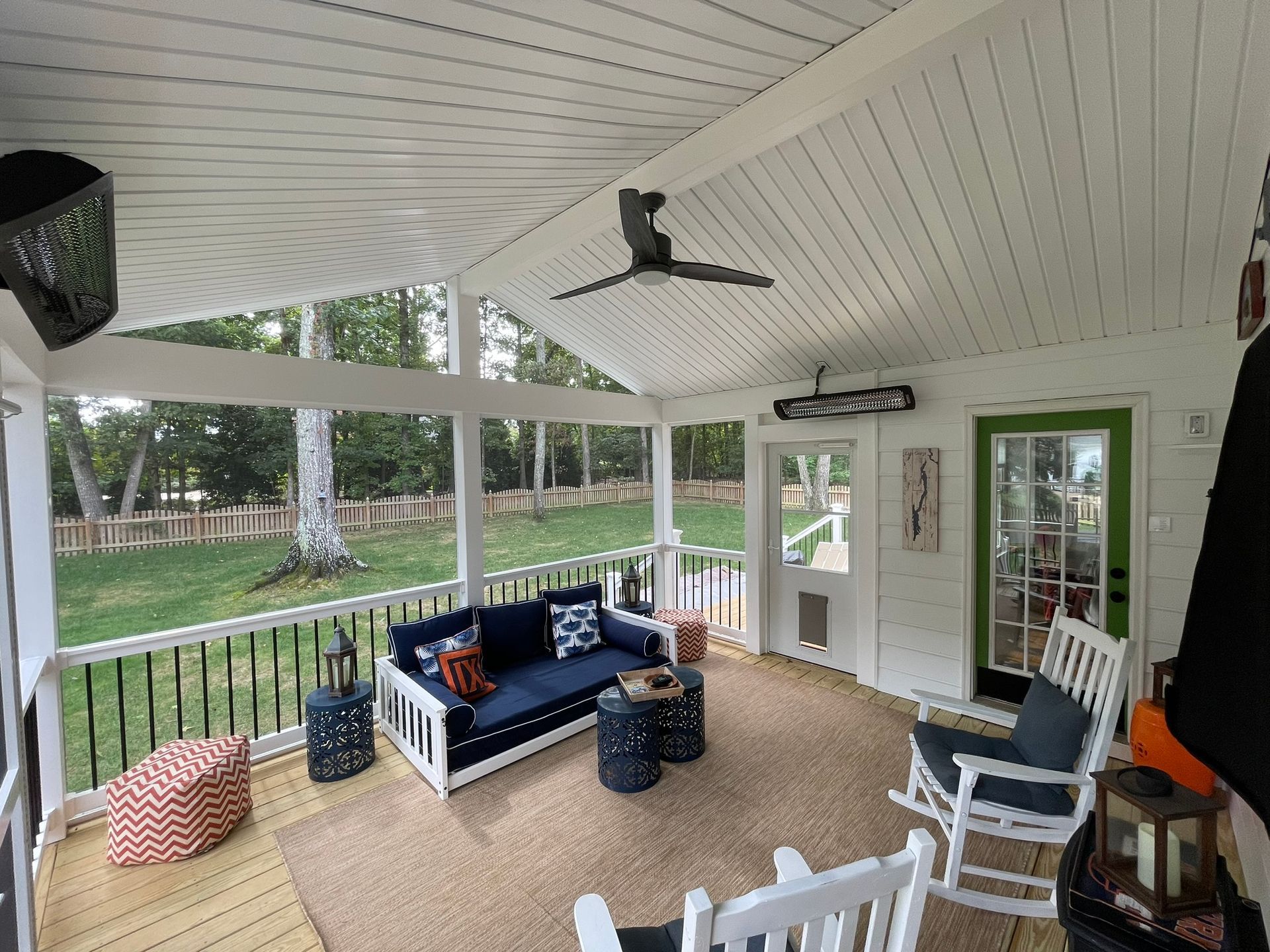 Covered porch with white ceiling, blue sofa, rocking chairs, and a view of a grassy yard and trees.