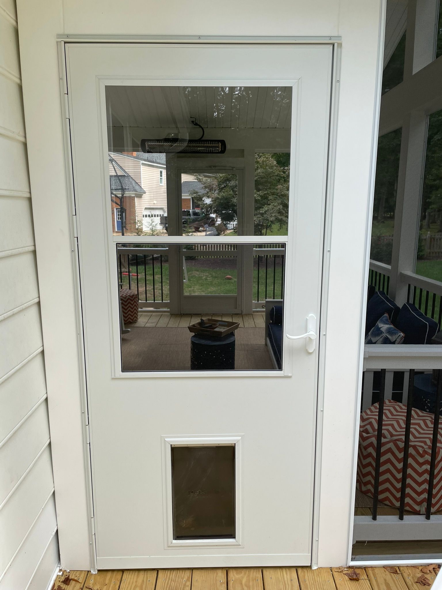 White door with glass panels and a pet flap on a porch, reflecting an outdoor deck and yard.
